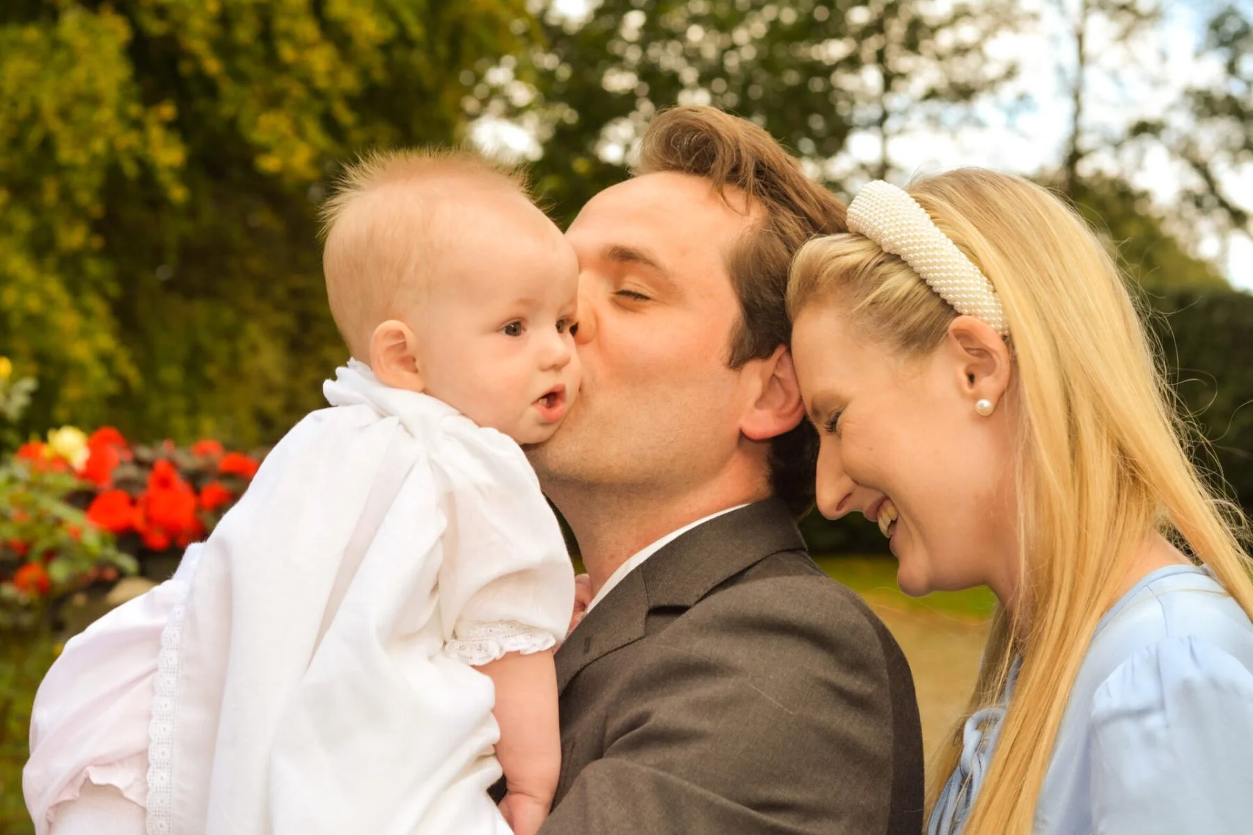 A family of three outdoors, with a man holding a young girl, and a woman smiling and leaning towards them.