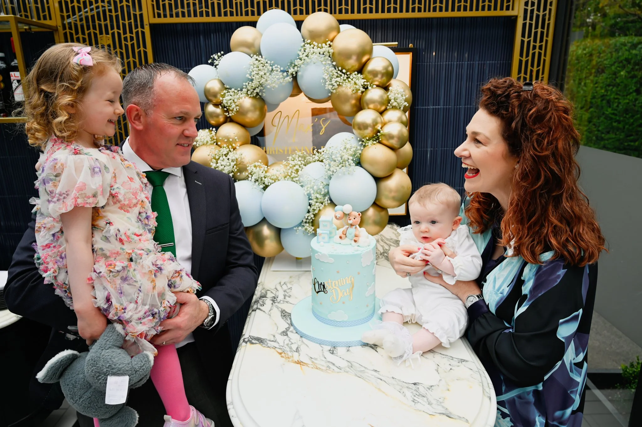 A baby dressed in white with a lace bonnet, sitting on an adult's lap during a baptism or christening ceremony inside a church.
