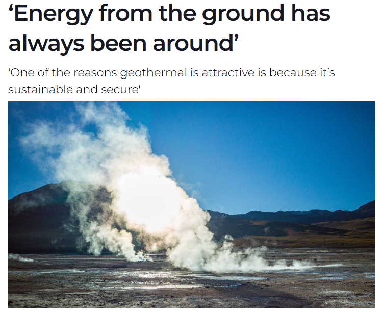Geyser erupting with steam and water in geothermal area with mountains in background.