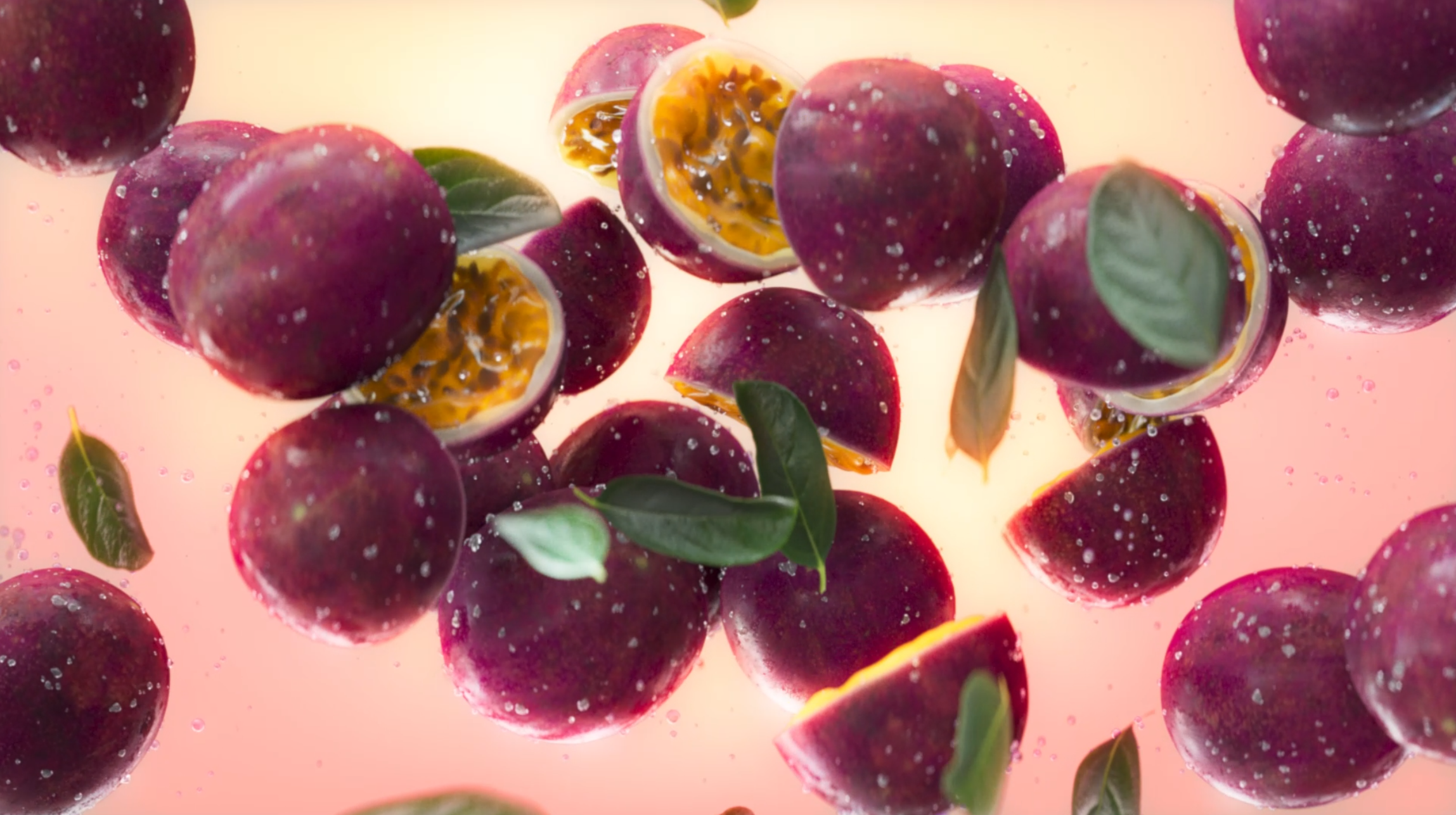 Several purple passion fruits, some cut open showing yellow pulp and seeds, floating on a pink background with green leaves and bubbles.