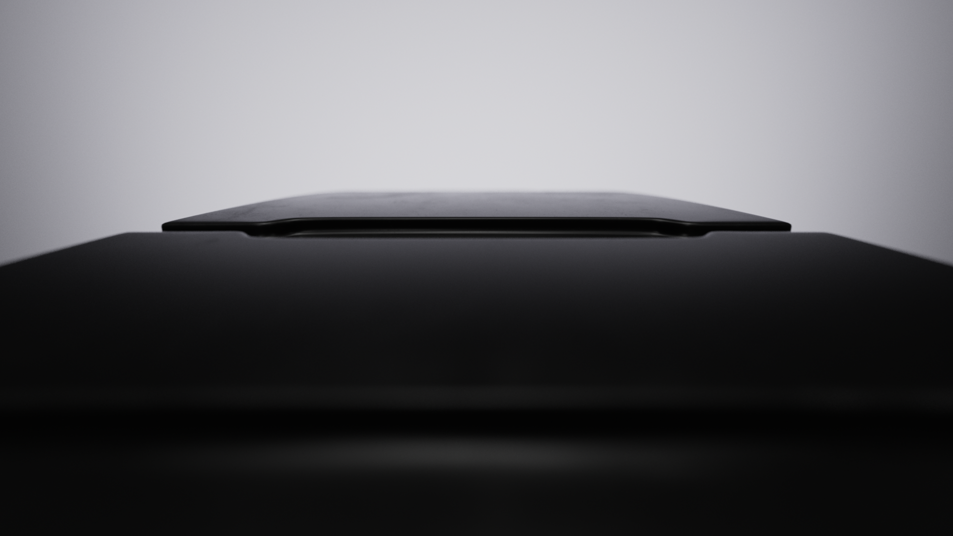 Close-up of a closed black laptop on a dark surface with a plain light grey background.