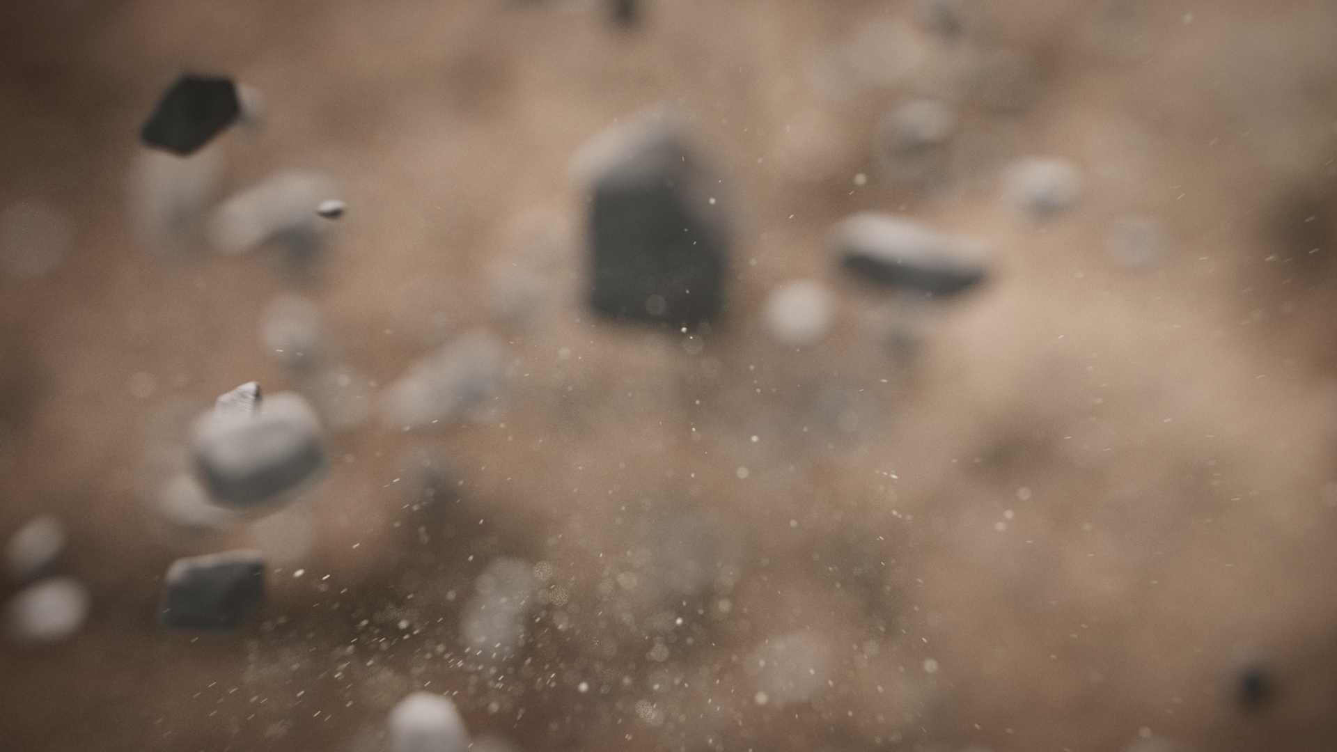 Close-up of small gray and black stones or particles suspended in air or dust, with a blurred background.