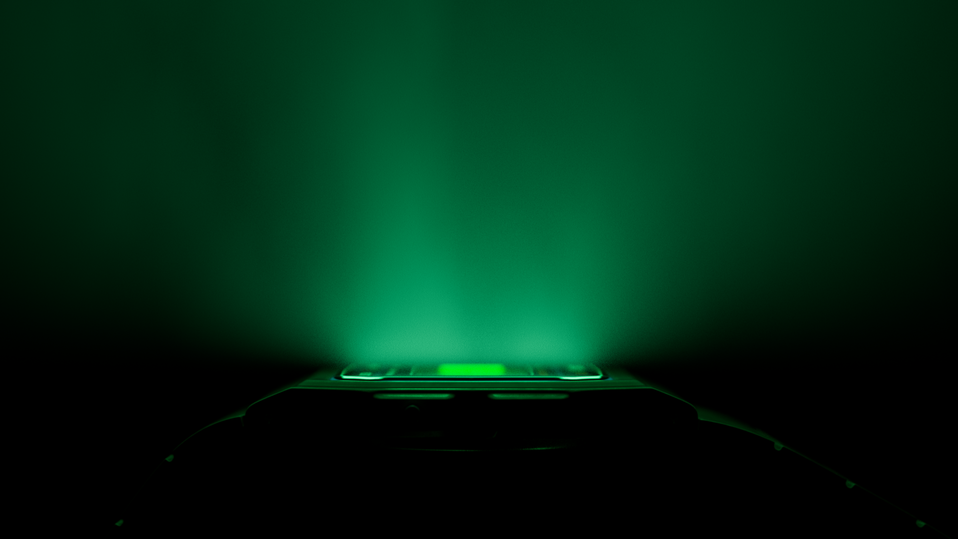 Close-up of a smartphone glowing with green illumination, with a dark background.