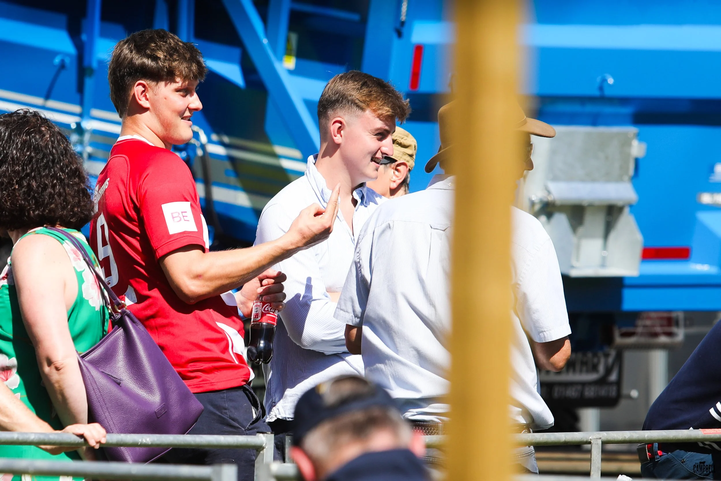 Group of people talking and smiling outdoors, with a blue construction vehicle in the background.
