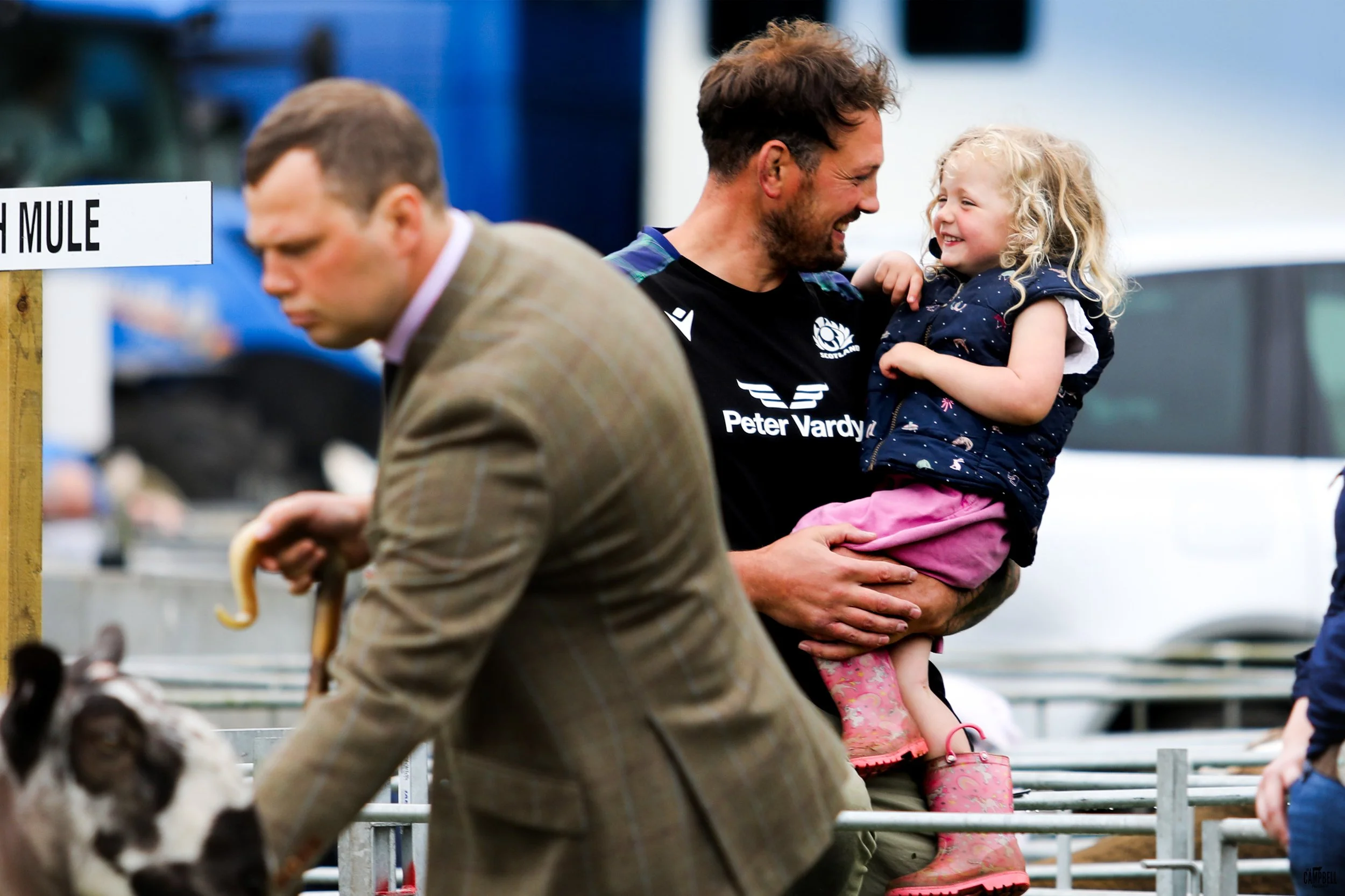 A man holding a smiling young girl at a fair or event.