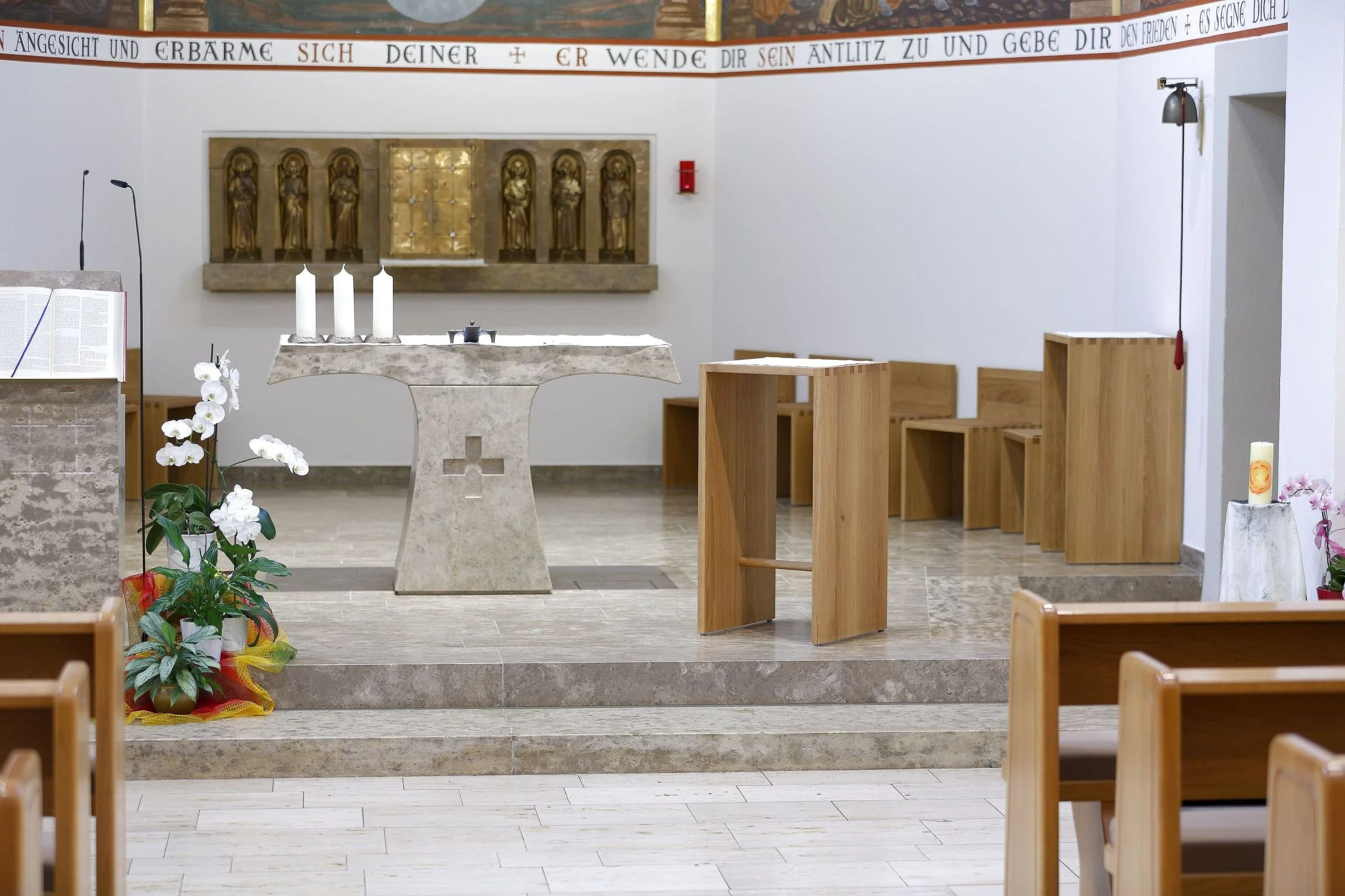Ein T-förmiger Altar in einer Kapelle von Vierzehnheiligen mit moderner schlichter Holzmöblierung mit Fingerzinken Verbindung, weißen Kerzen und Blumen.