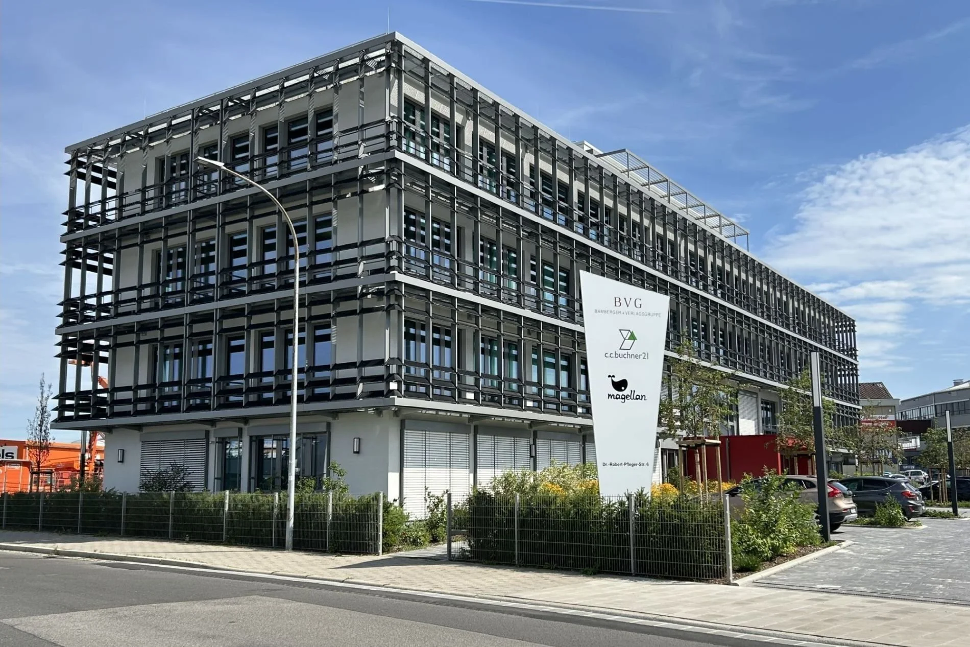 Mehrstöckiges modernes Bürogebäude mit PV-Modulen vor der Fassade, die auch als Sonnenschutz dienen. Davor einer weißer BVG Werbepylon.