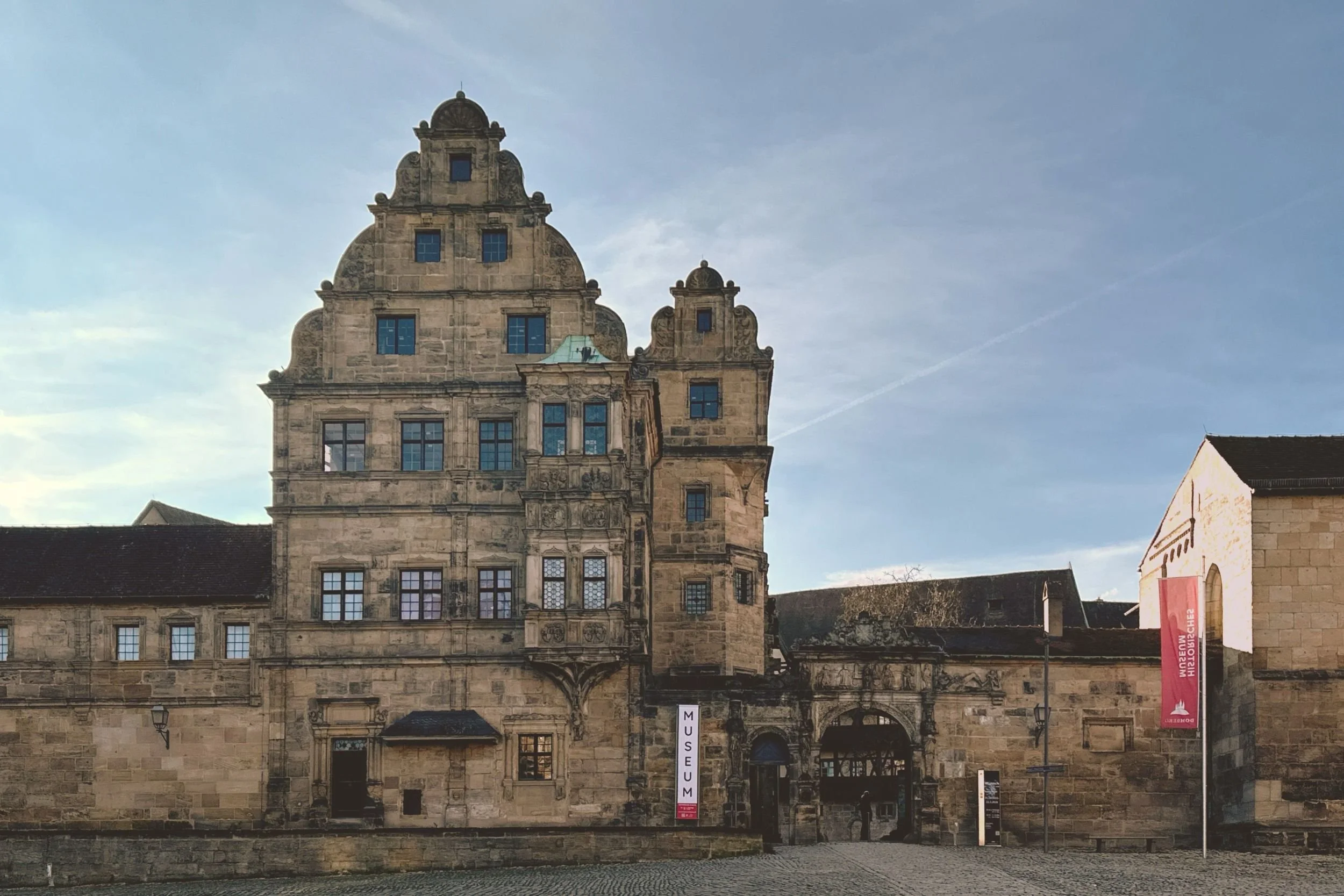historisches hohes Gebäude neben dem Eingangstor in einen Hof mit blauem Himmel.