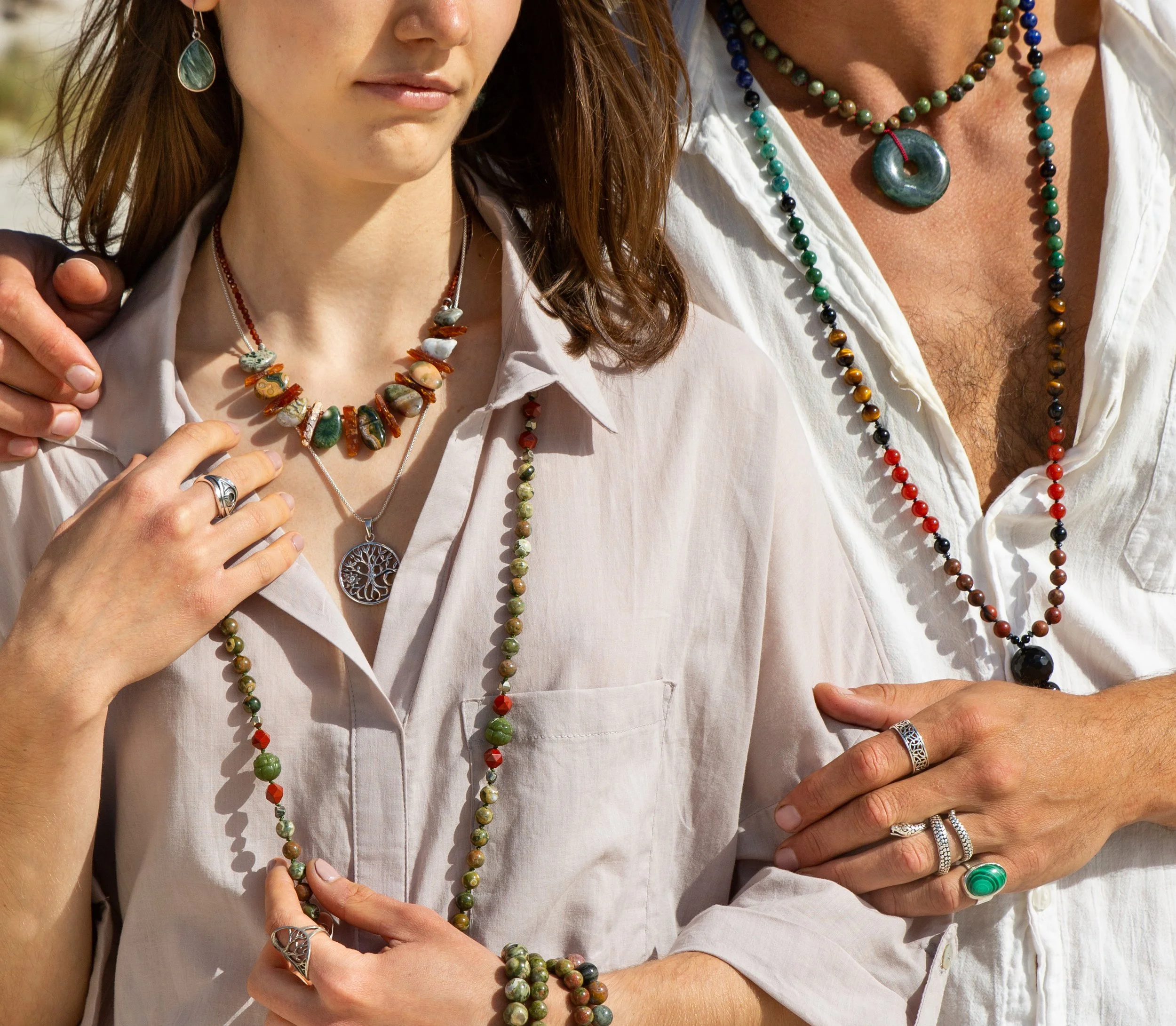 Two people wearing multiple colorful beaded necklaces and rings, with one person having an arm around the other.