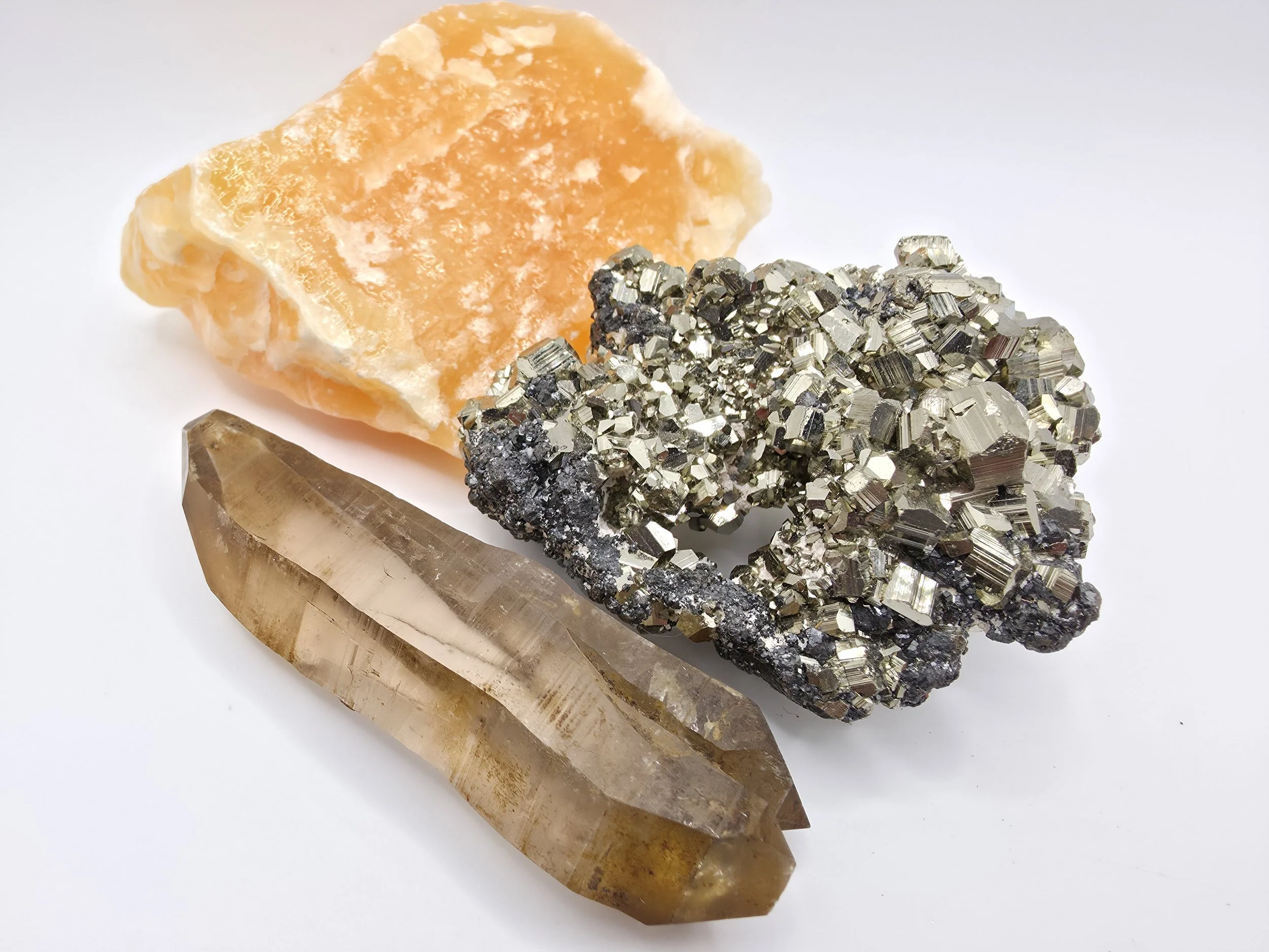 Three mineral specimens: a piece of orange calcite with white veining, a cluster of metallic pyrite cubic crystals, and a long, translucent, brownish quartz crystal.