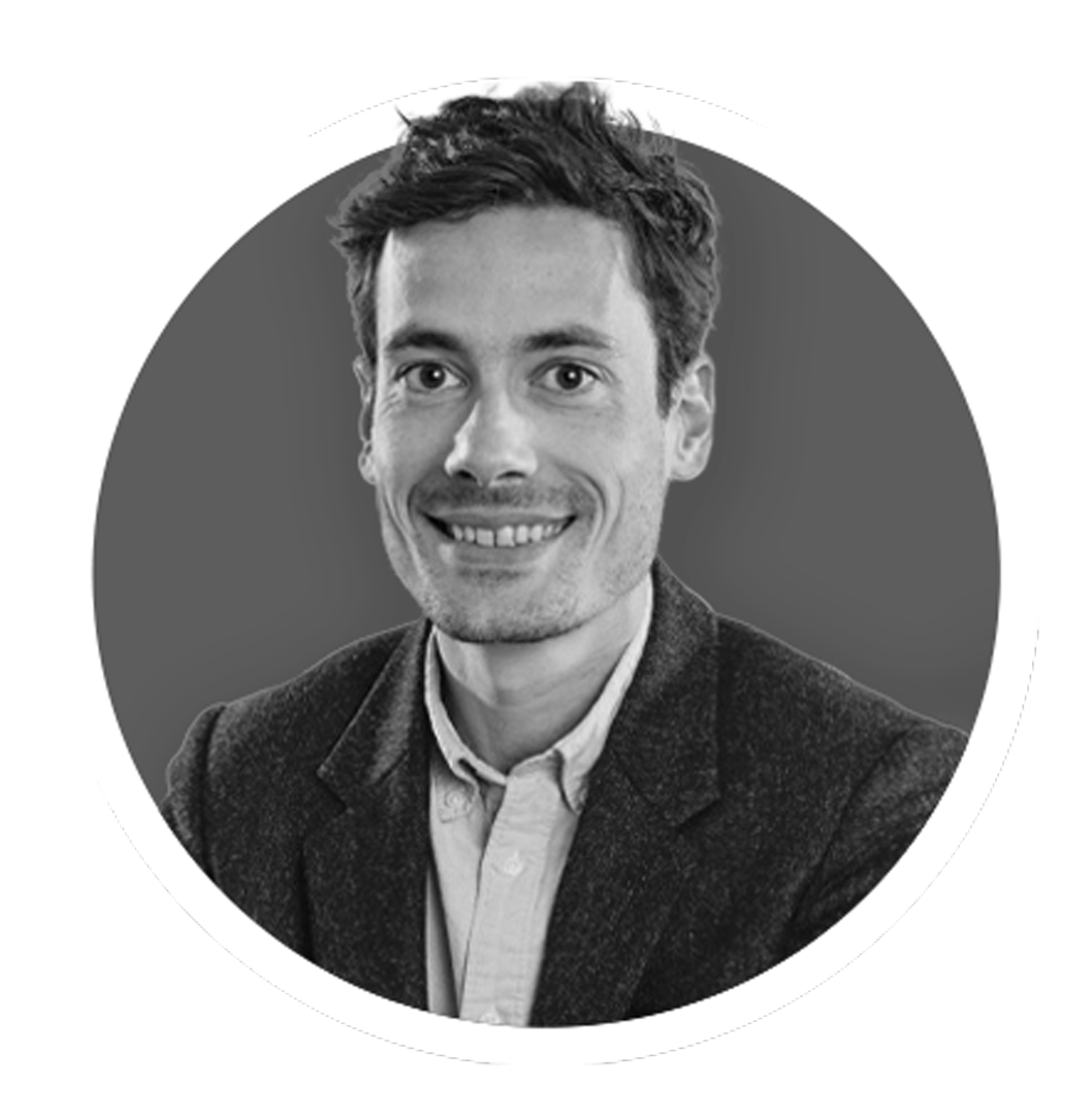 Black and white portrait of a smiling man wearing a tweed jacket and shirt, with a gray background.