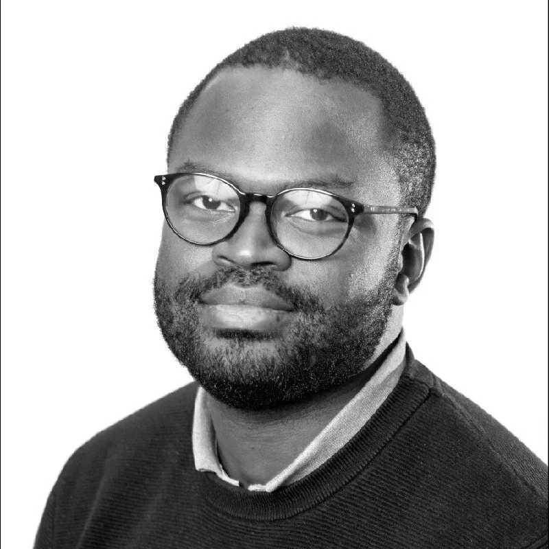 Portrait en noir et blanc d'un homme portant des lunettes, une barbe et un pull, regardant vers la caméra.