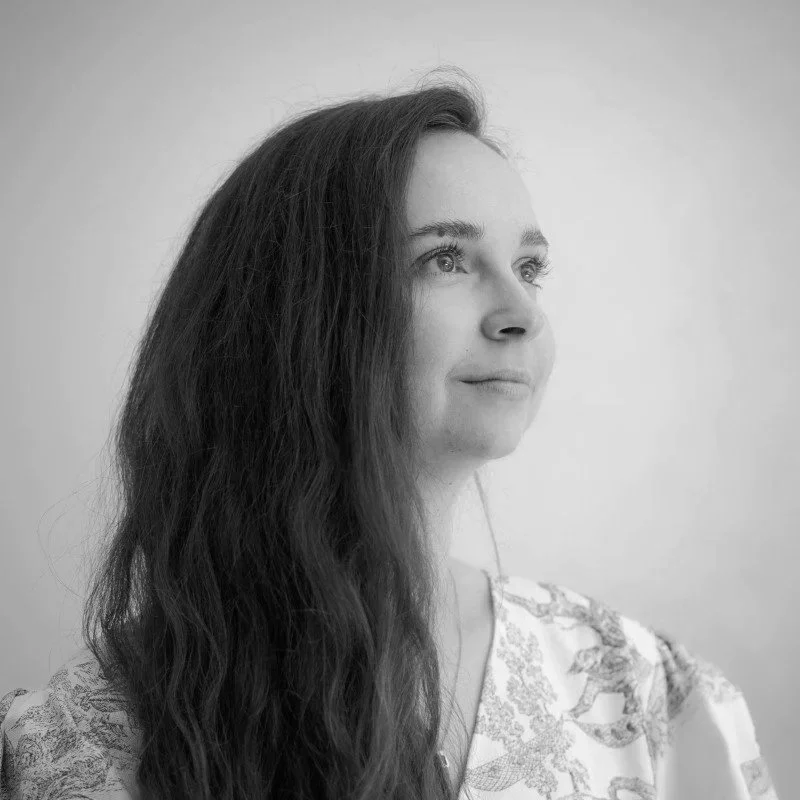 Jeune femme avec des cheveux longs et ondulés, regardant vers la droite, dans une pose pensive, en noir et blanc.