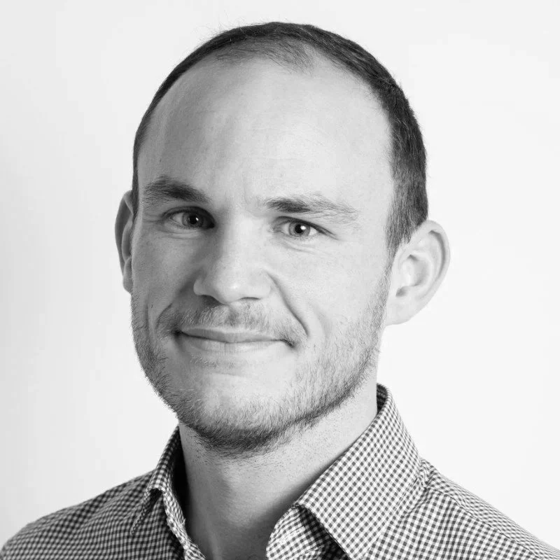 Portrait en noir et blanc d'un homme avec une expression douce, portant une chemise à carreaux.