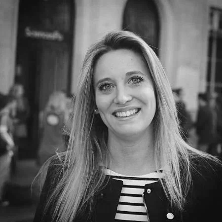 Une femme souriante avec long cheveux, portant un vêtement à rayures, en ville.