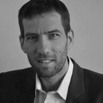 Portrait en noir et blanc d'un homme en costume et chemise blanche, souriant légèrement.