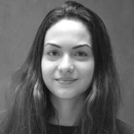 Portrait en noir et blanc d'une jeune femme avec des cheveux longs et ondulés, souriant légèrement, fond neutre.