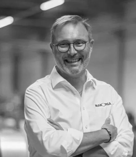 Un homme souriant portant des lunettes et une chemise blanche dans un environnement intérieur.