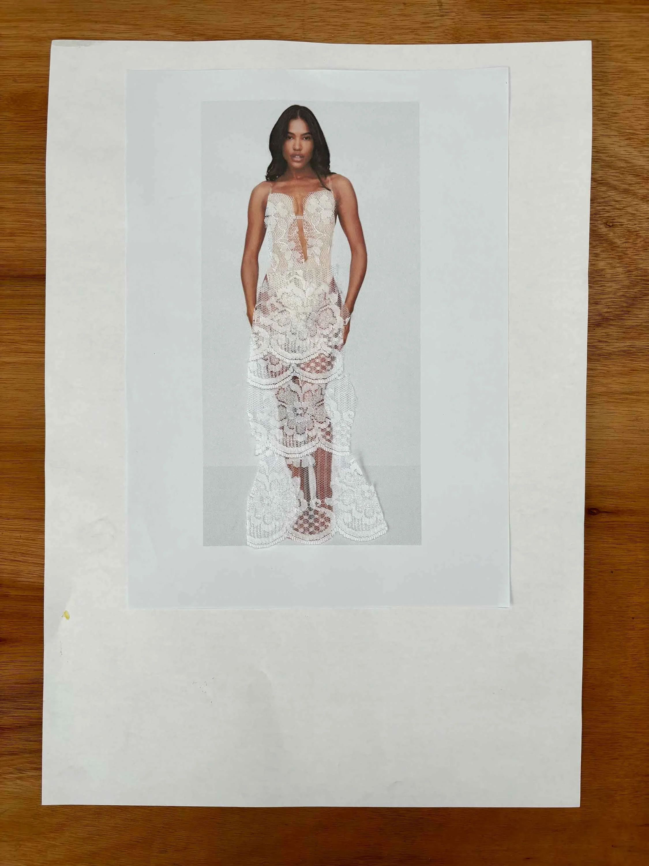 A printed photo of a woman wearing a white lace dress, placed on a piece of white paper on a wooden surface.