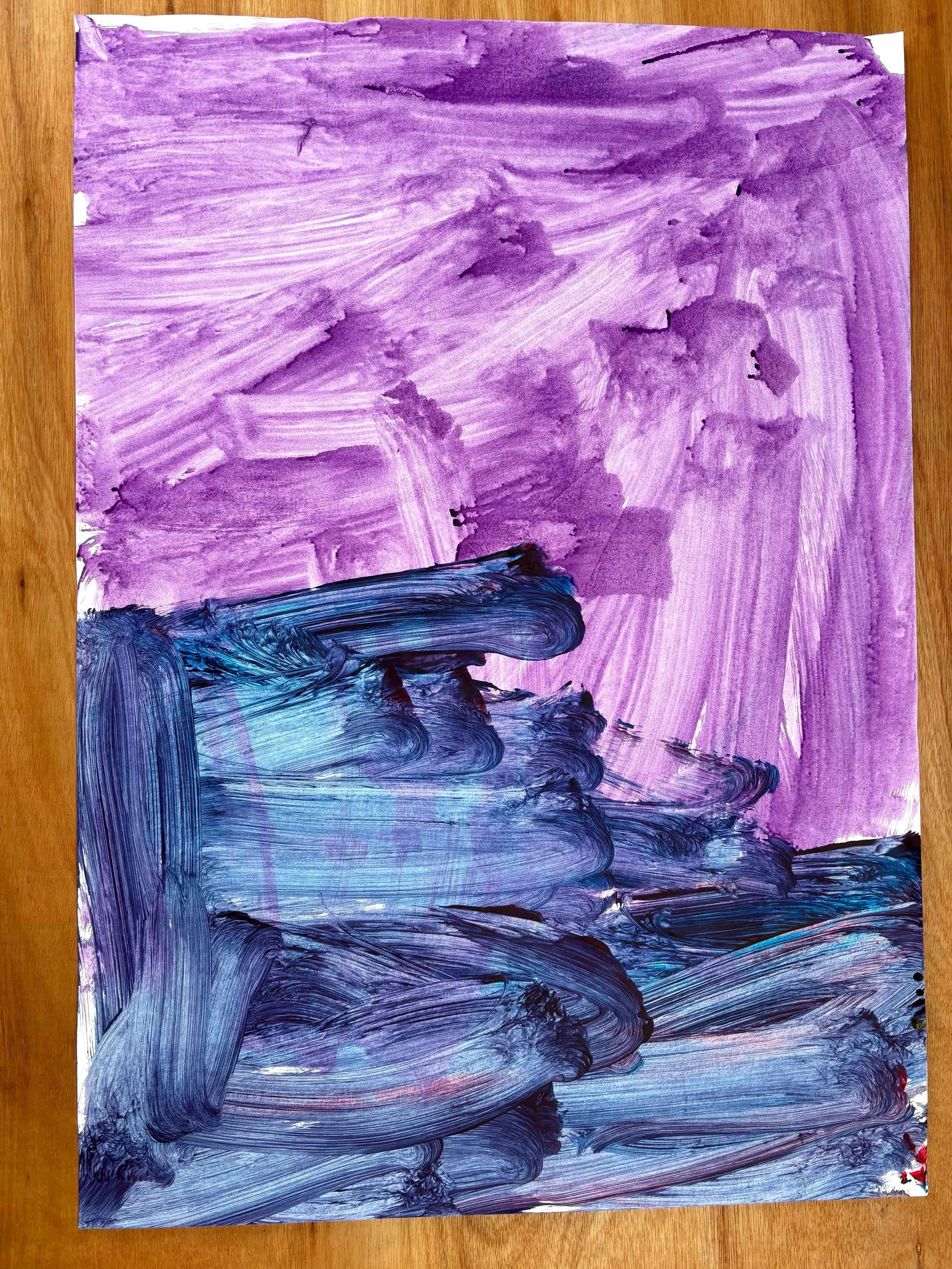 Abstract painting with purple and blue brushstrokes on paper placed on a wooden surface.