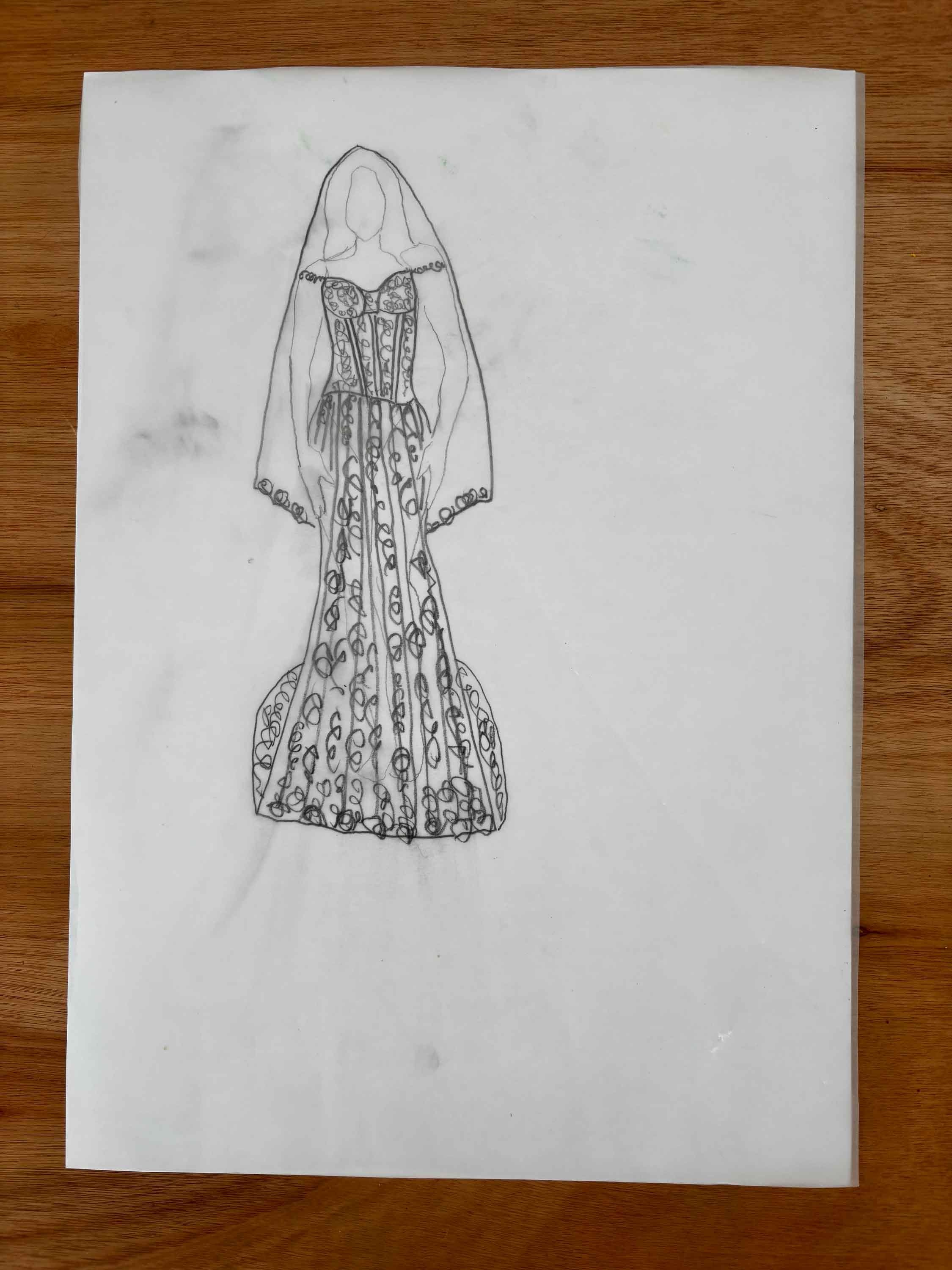 A hand-drawn sketch of a woman wearing a long, elaborate dress and cape with detailed patterns, on a white sheet of paper placed on a wooden surface.