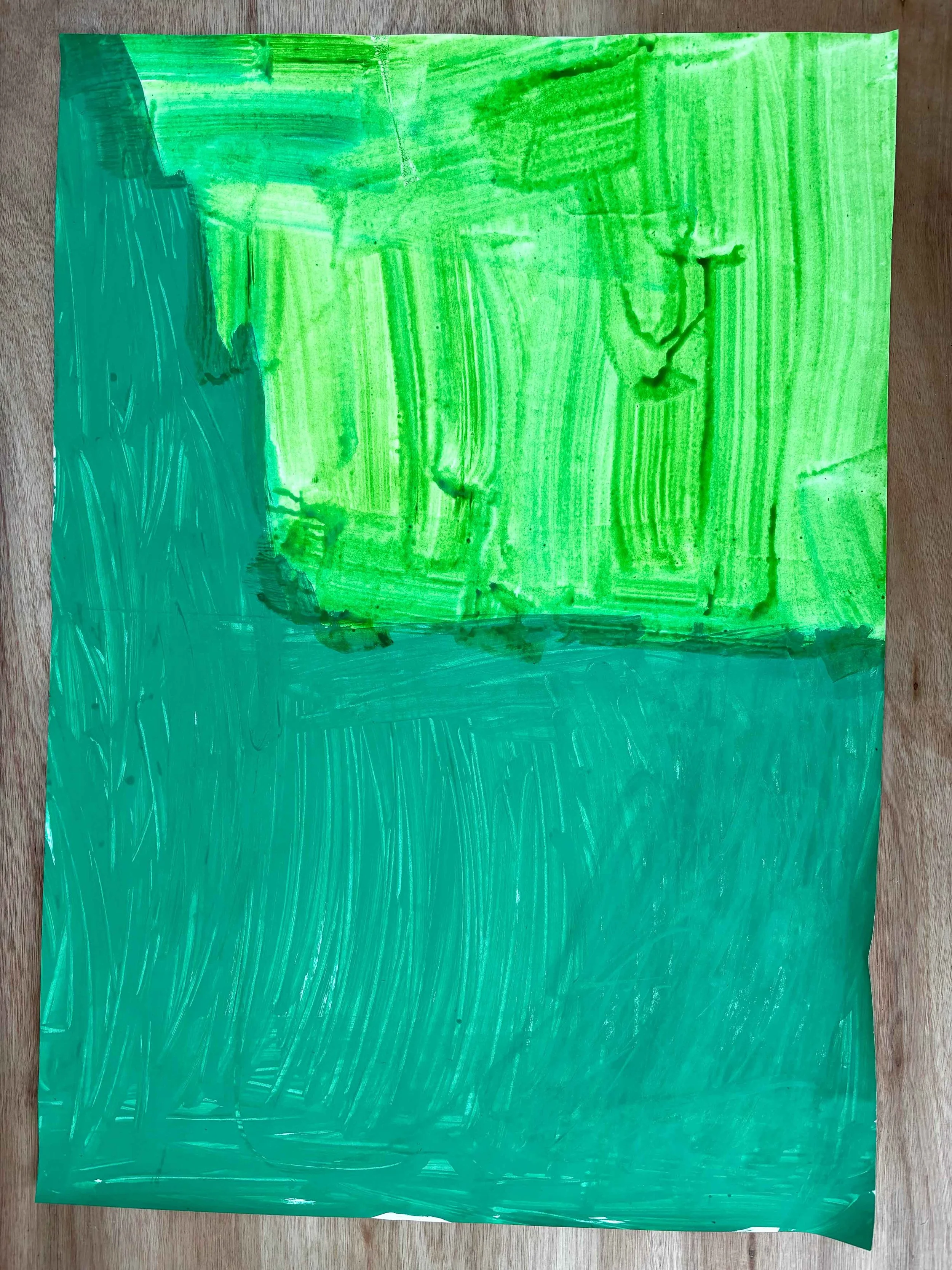 A sheet of paper painted with green watercolor, showing brushstrokes and texture, placed on a wooden surface.