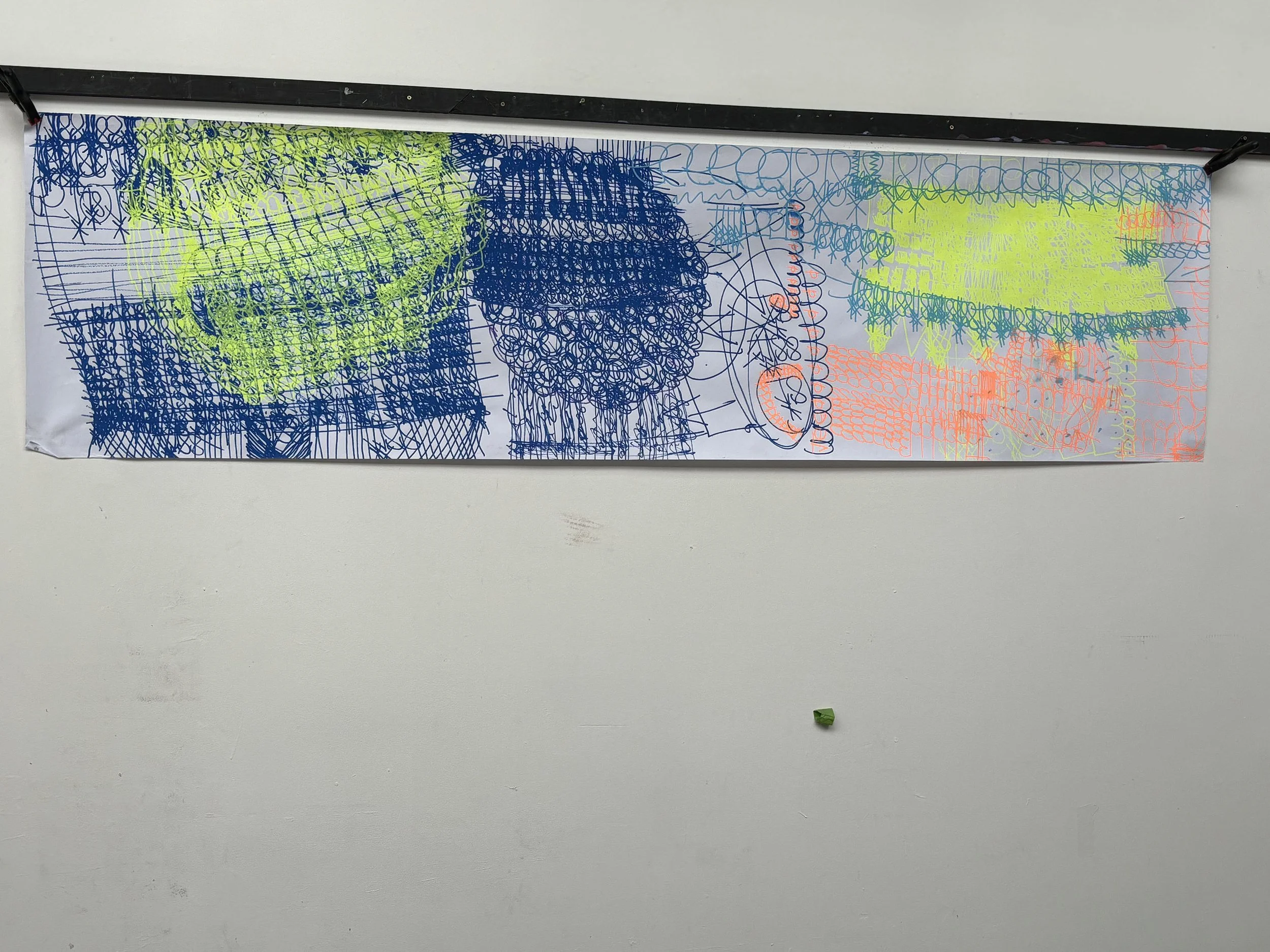 A whiteboard with colorful marker scribbles in blue, yellow, orange, and green, with a black border at the top and a small green object on the floor below.