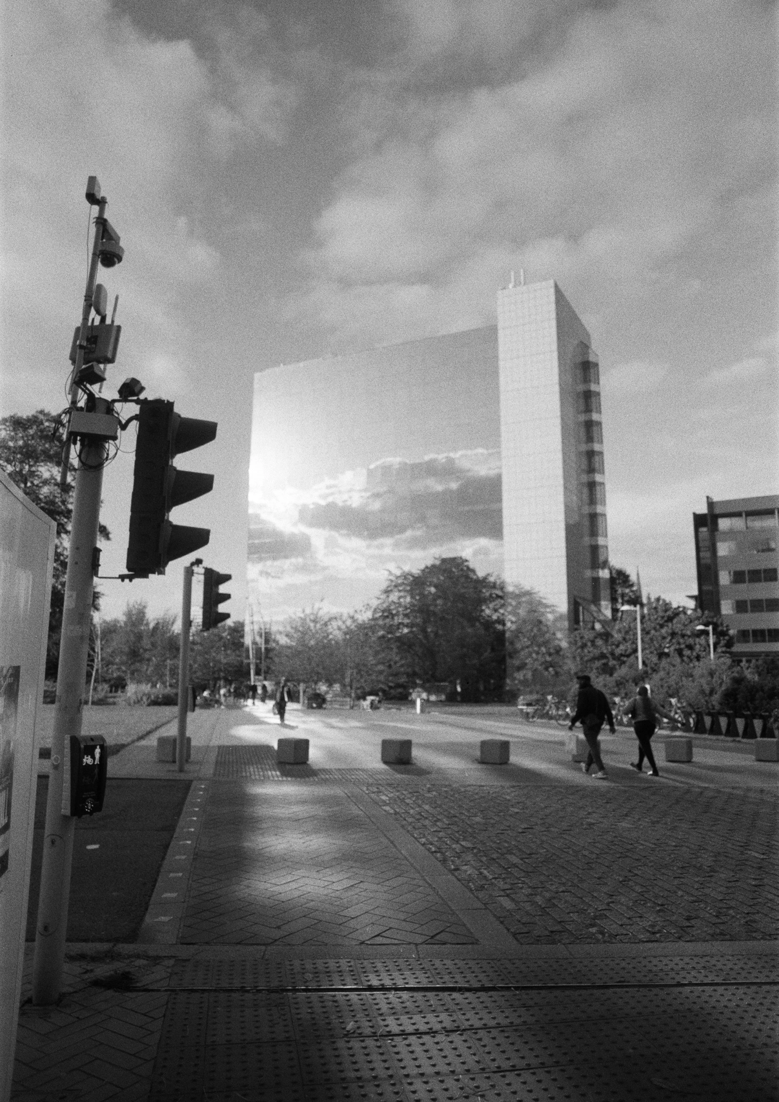 Urban street scene with pedestrian crosswalk, traffic lights, and tall modern building in the background, black and white photograph.