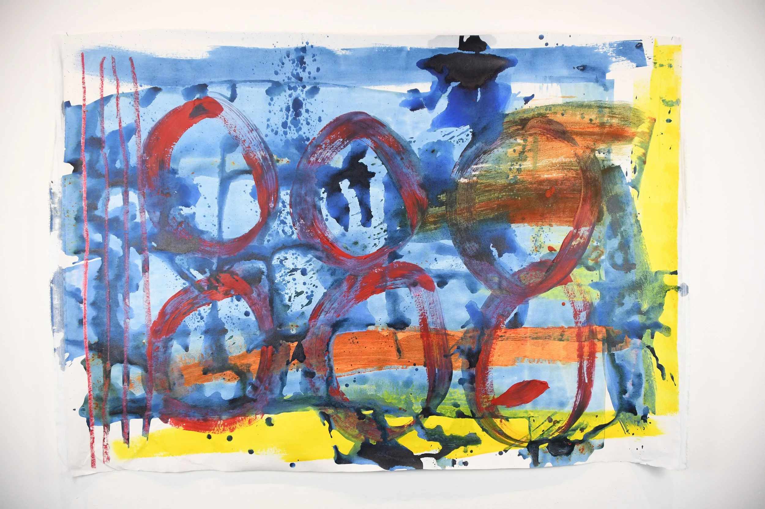 Abstract painting with blue, red, yellow, and black splashes and strokes, including large red circles and vertical red lines on the left.