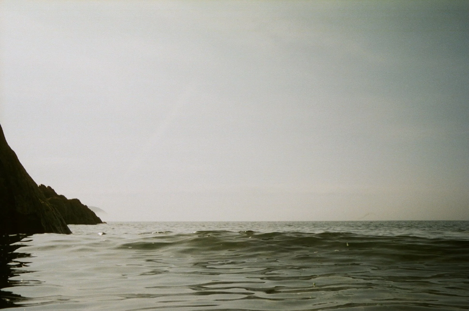 Calm ocean water with gentle waves near a rocky coastline, under a cloudy sky.