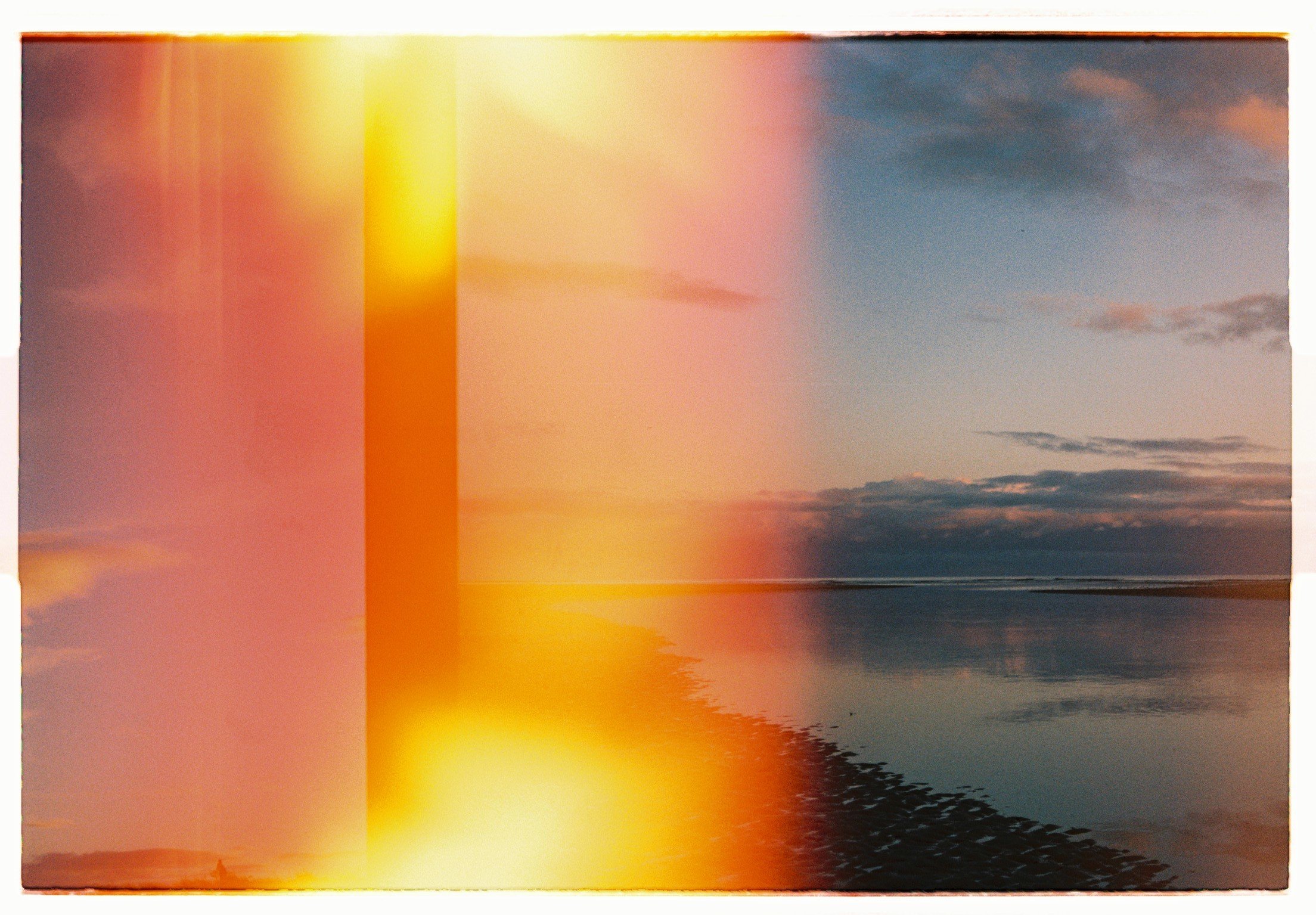 Photograph of a sunset over a water body with clouds in the sky, but image has light streaks and color distortions across it.