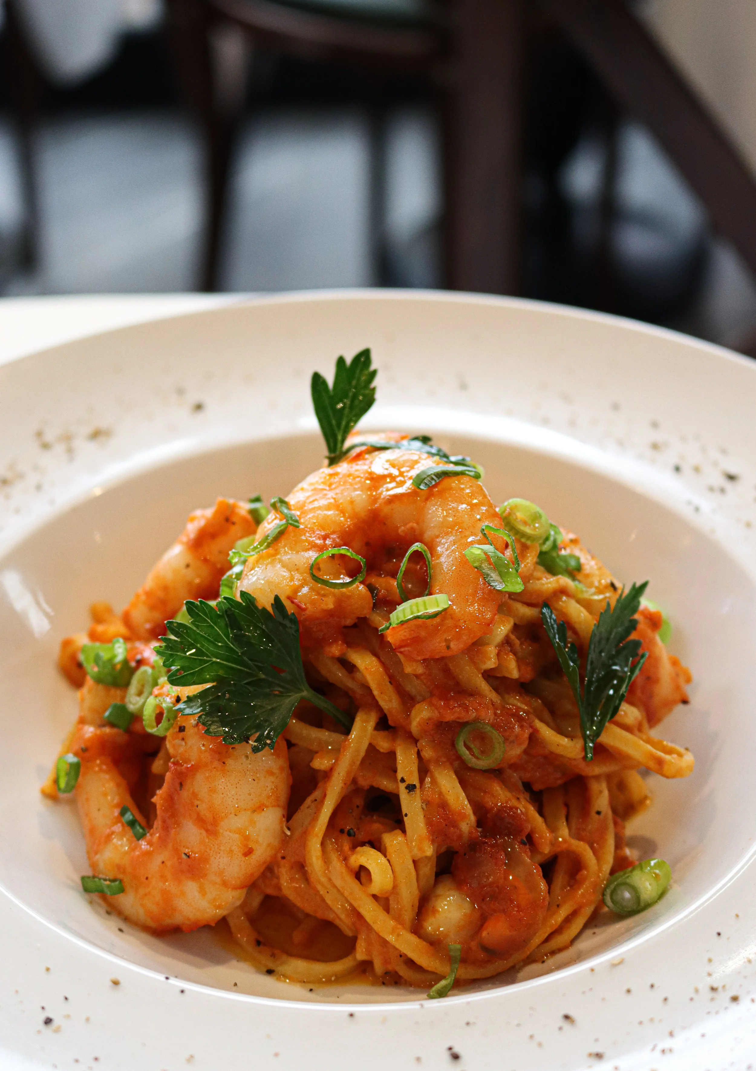 Plat de pâtes aux crevettes, garnies de persil et d'oignons verts, dans un bol blanc.