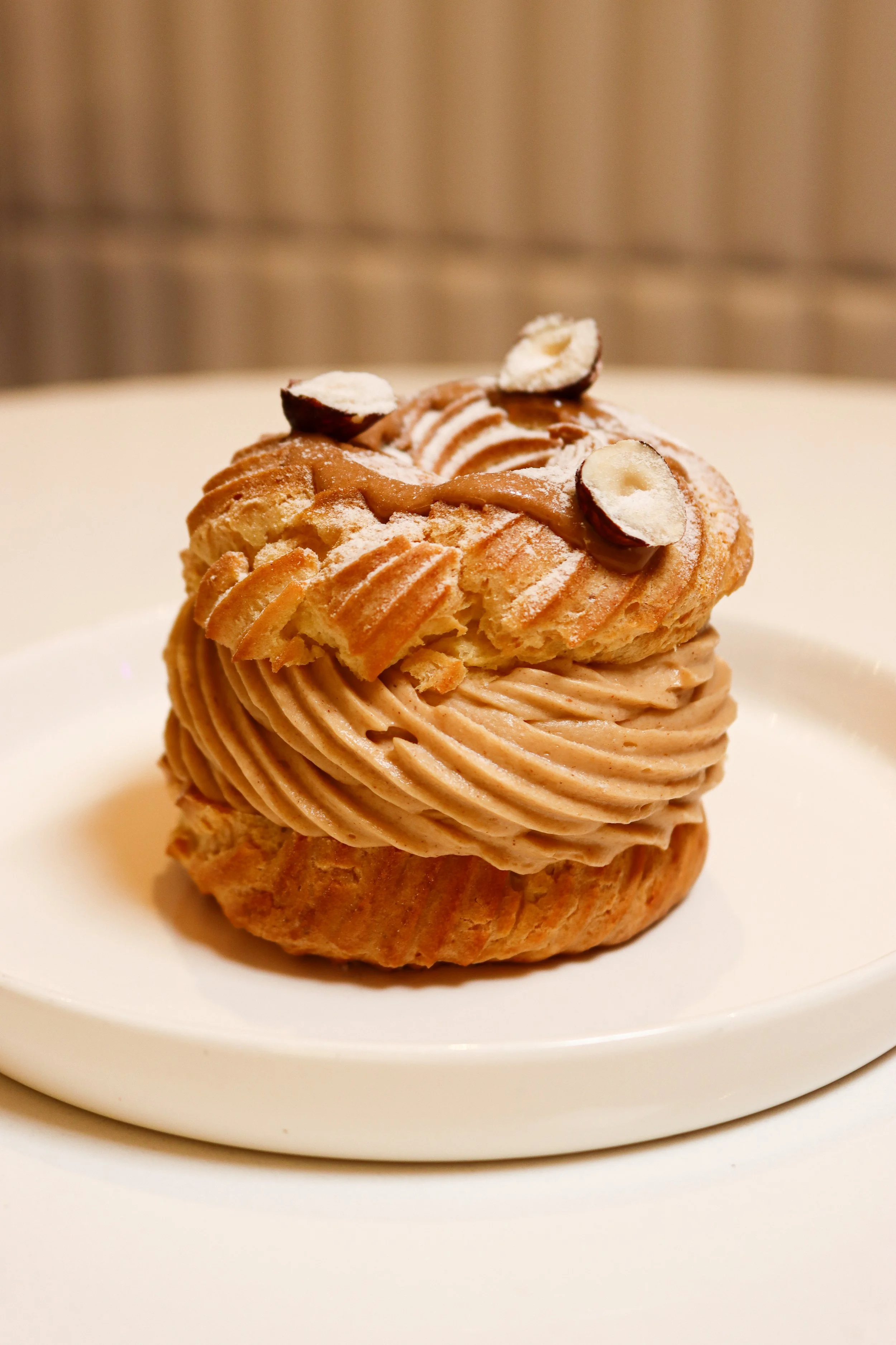 Un cupcake avec une base de biscuit, garni de crème de couleur marron clair, décoré avec des éclats d'amande et des morceaux de chocolat. Le cupcake est présenté sur une assiette blanche.
