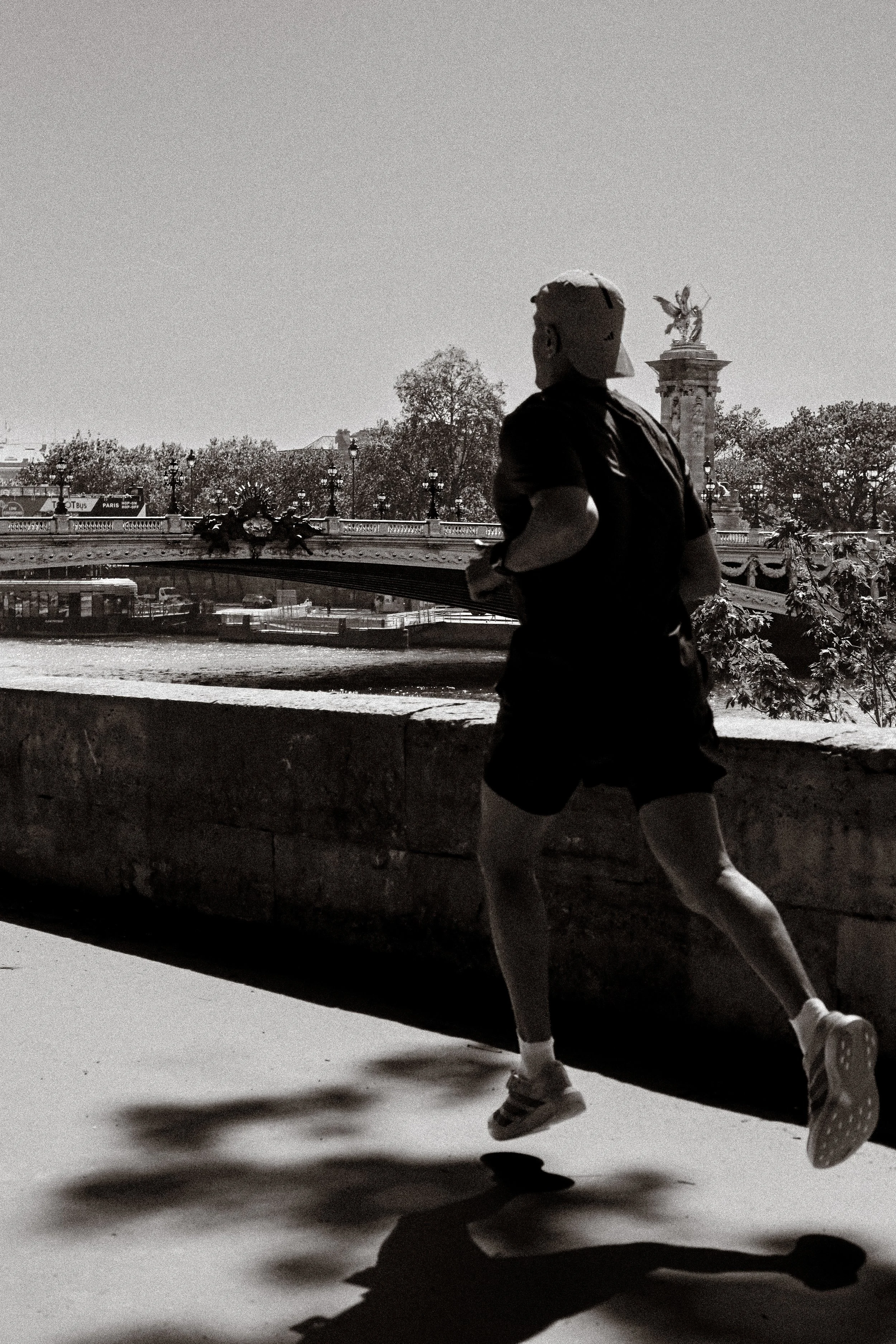Une silhouette d'un coureur en mouvement, au premier plan, avec le pont Alexandre III en arrière-plan, photographie en noir et blanc.