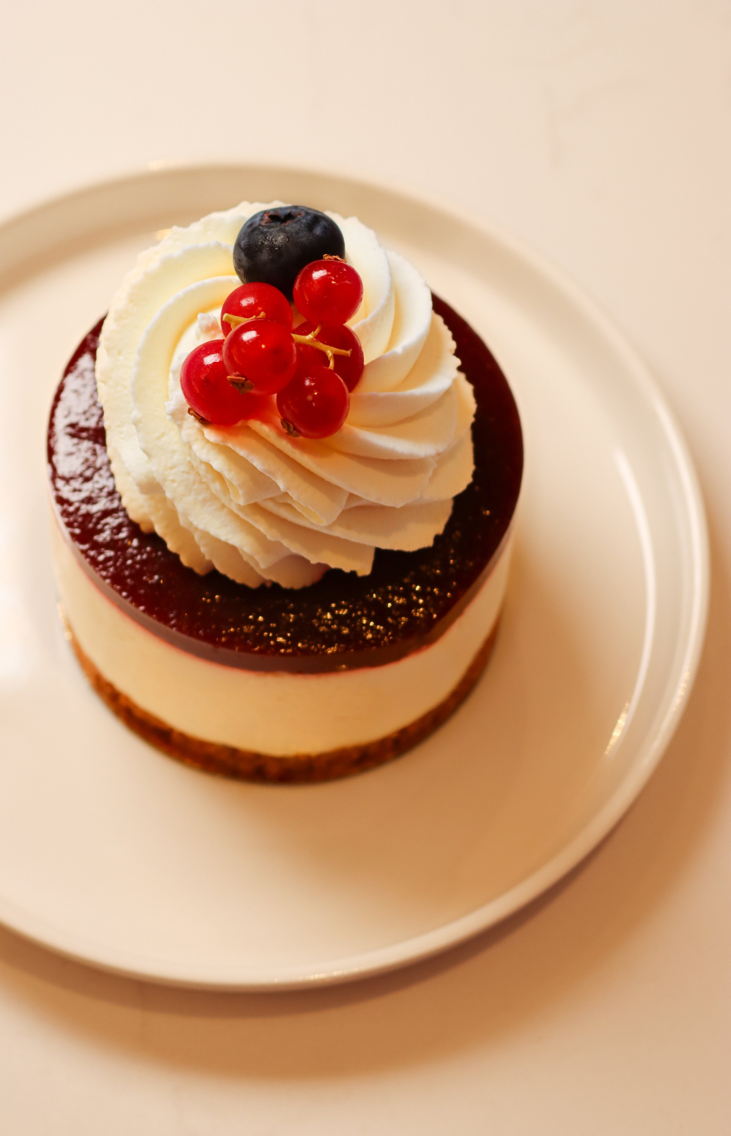 Gâteau avec une couche de crème blanche, garniture de fruits rouges, myrtille et groseille, sur une assiette blanche.