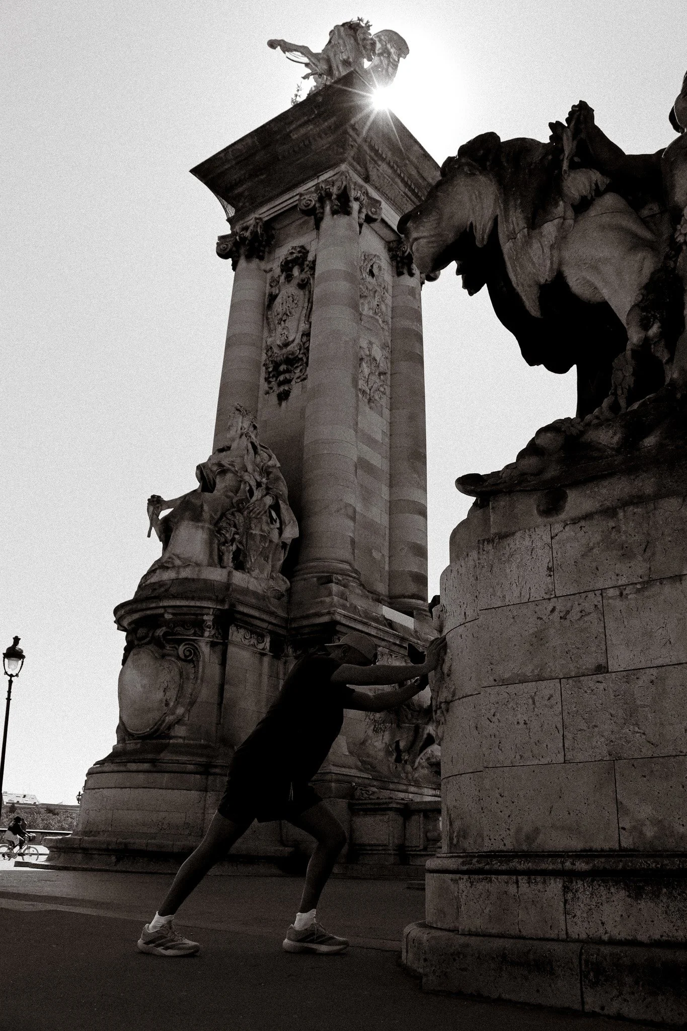 Photographie de sport: Une personne en train d'exécuter un exercice de fitness près d'une sculpture du Pont Alexandre III à Paris sous le soleil éblouissant. en noir et blanc.