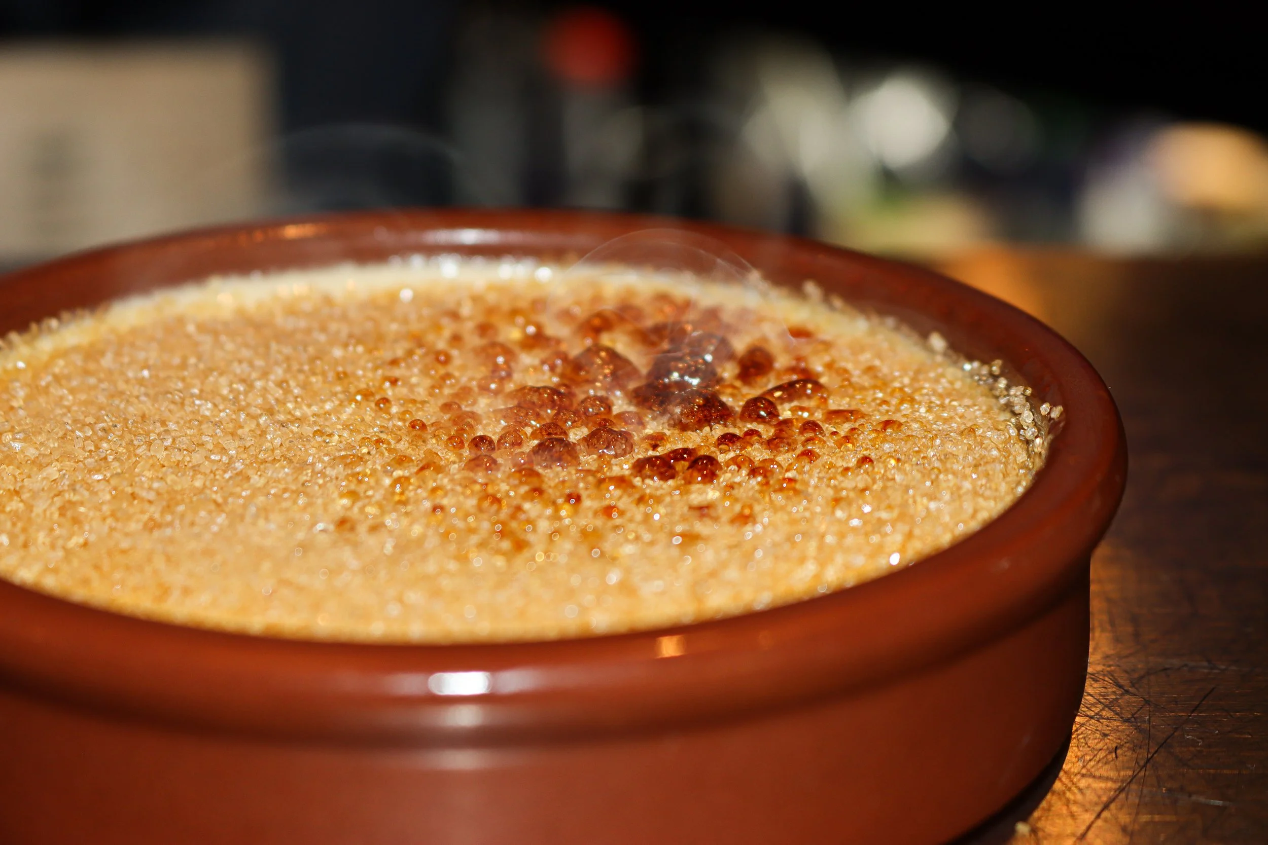 Une tasse en terre cuite contenant un café crémeux avec une mousse dorée, située sur une surface en bois.