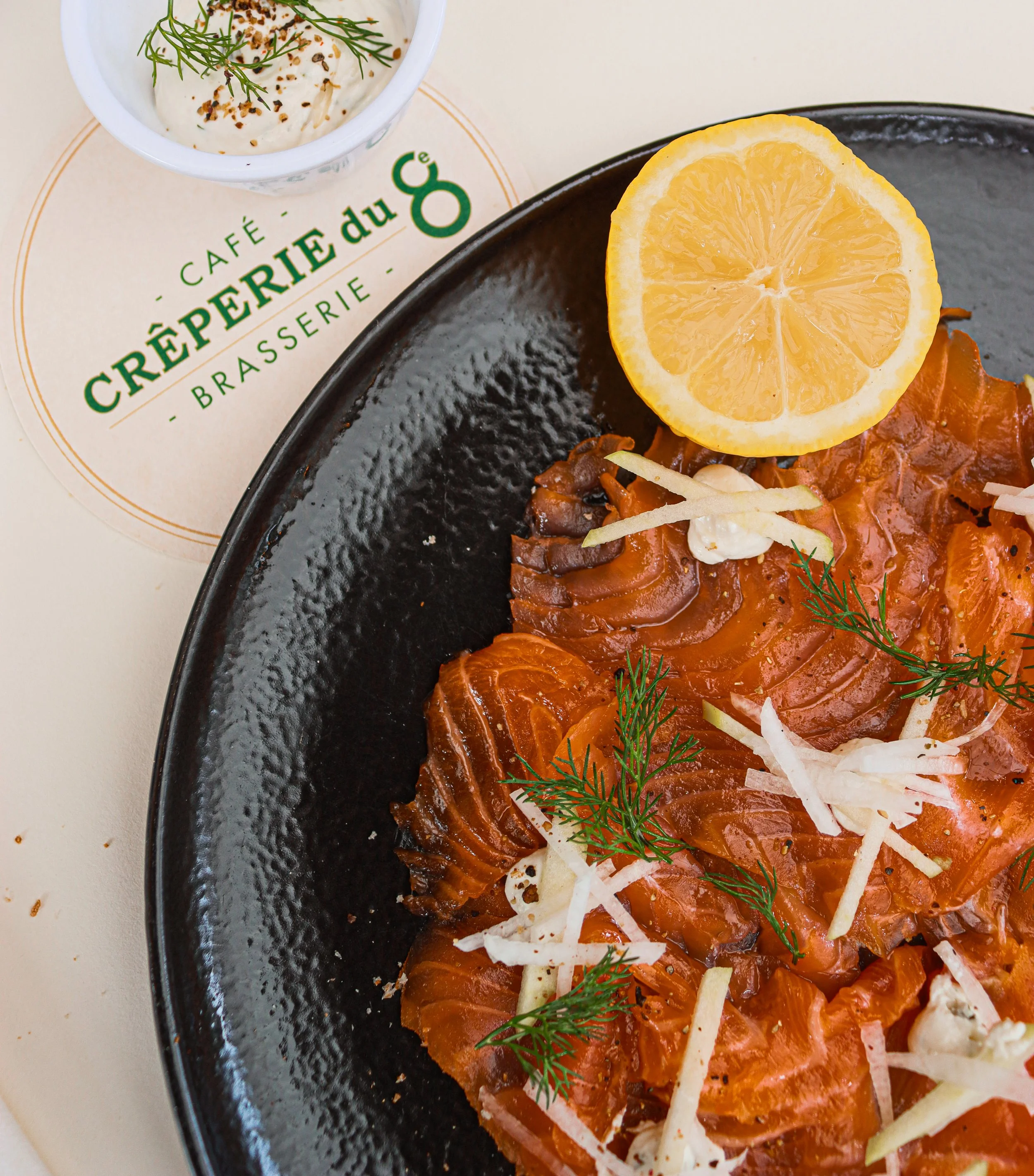 Tranches de saumon fumé garnies de dill, de lanières de légumes et d'une tranche de citron sur une assiette noire.