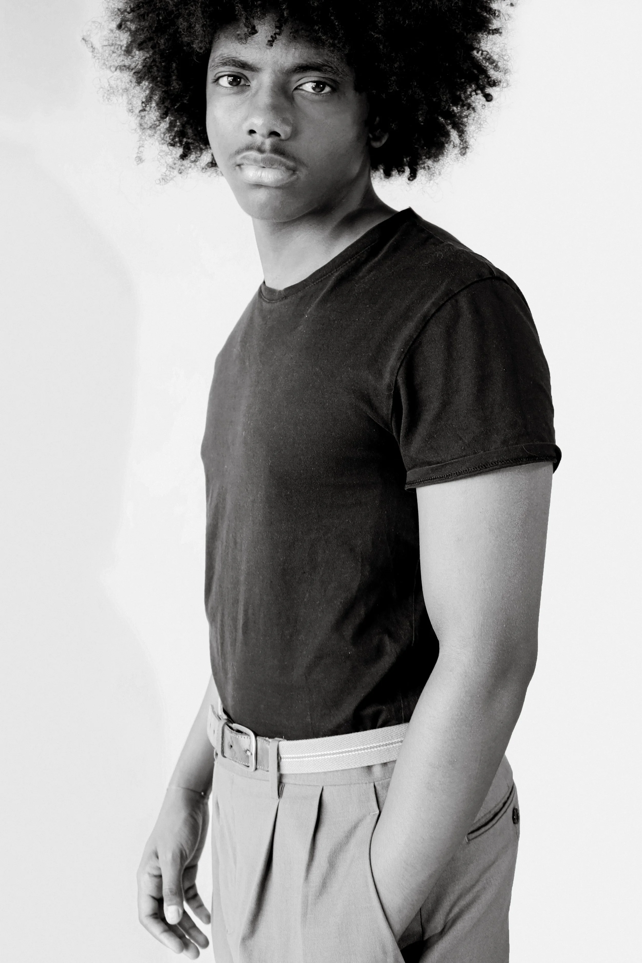 Portrait en noir et blanc d'une personne avec des cheveux bouclés et une tenue élégante, visible de la tête aux hanches, contre un fond blanc.