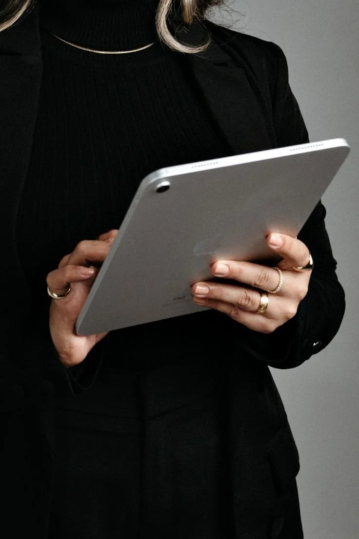 Persona sosteniendo una tableta plateada, vistiendo ropa negra y usando anillos y collar
