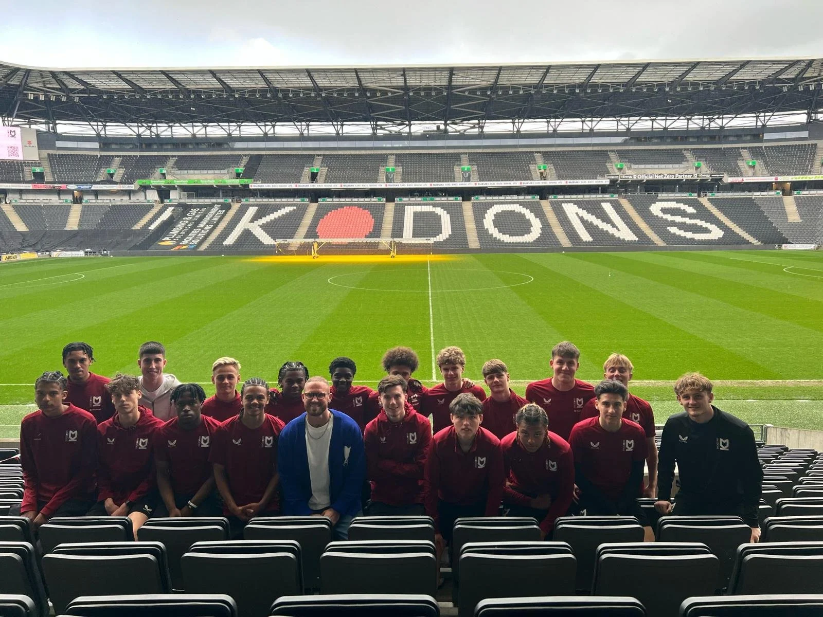 A soccer team posing for a photo inside a stadium with the field and stands in the background, with the stands spelling out 'KØBENHAVN'.