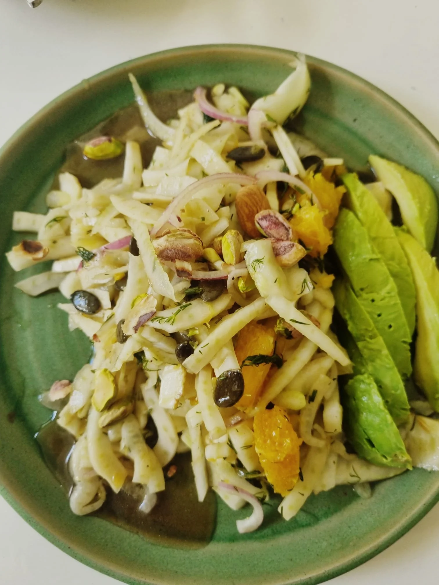 Assiette de vegetables avec des feuilles de laitue, agrumes, graines et noix, servie dans une assiette verte.