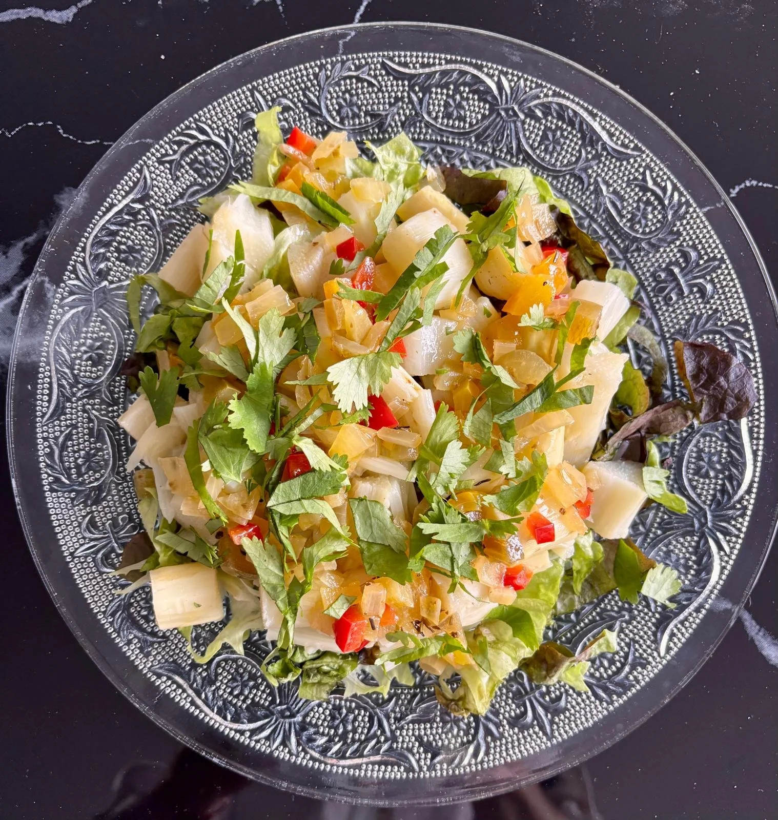 Salade de légumes dans un plat en verre décoratif, avec des morceaux de céleri, poivron rouge, et herbes fraîches.