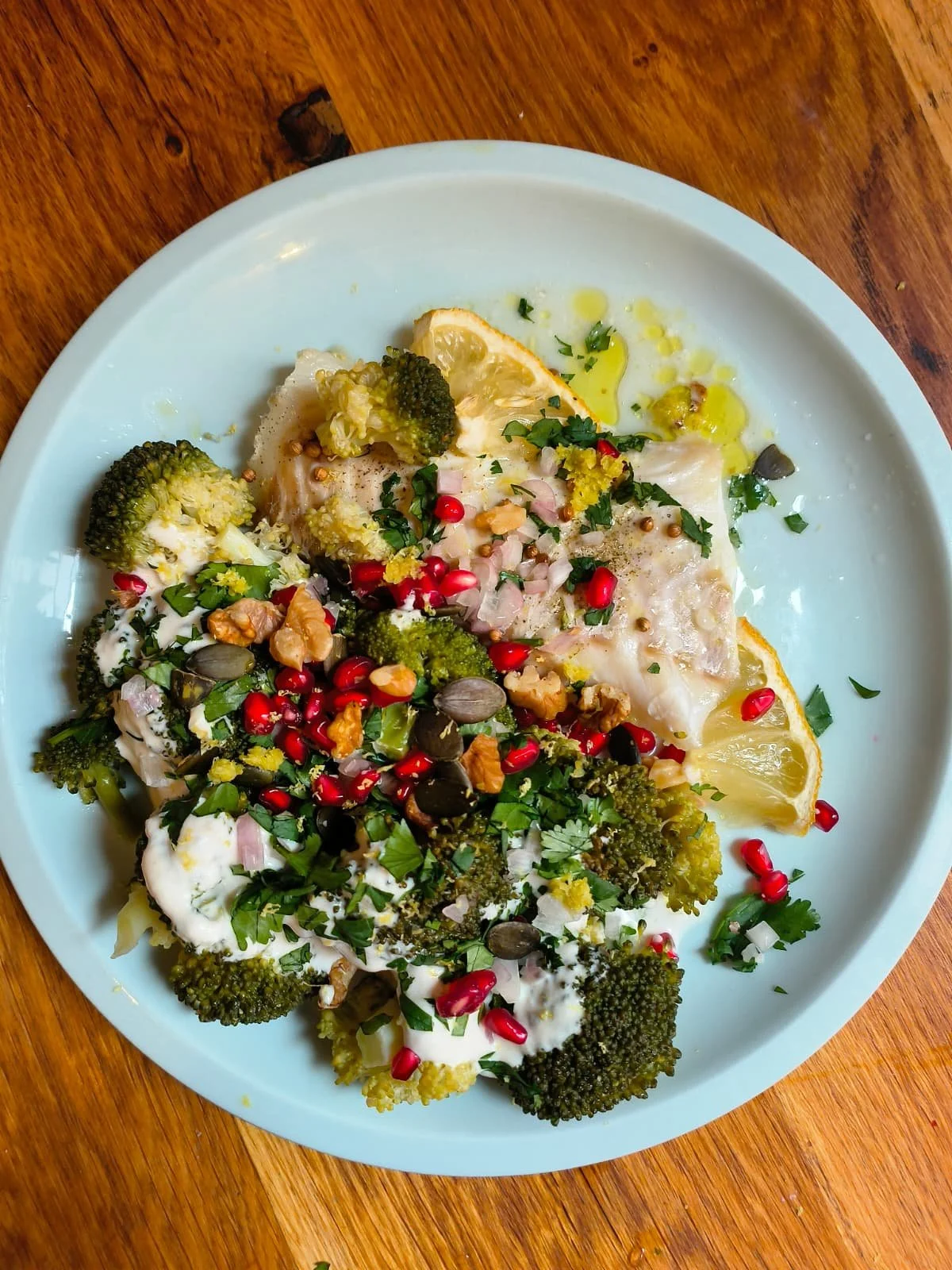 Assiette de poisson avec brocolis, citron, sauce blanche, herbes, noix, graines et grenade