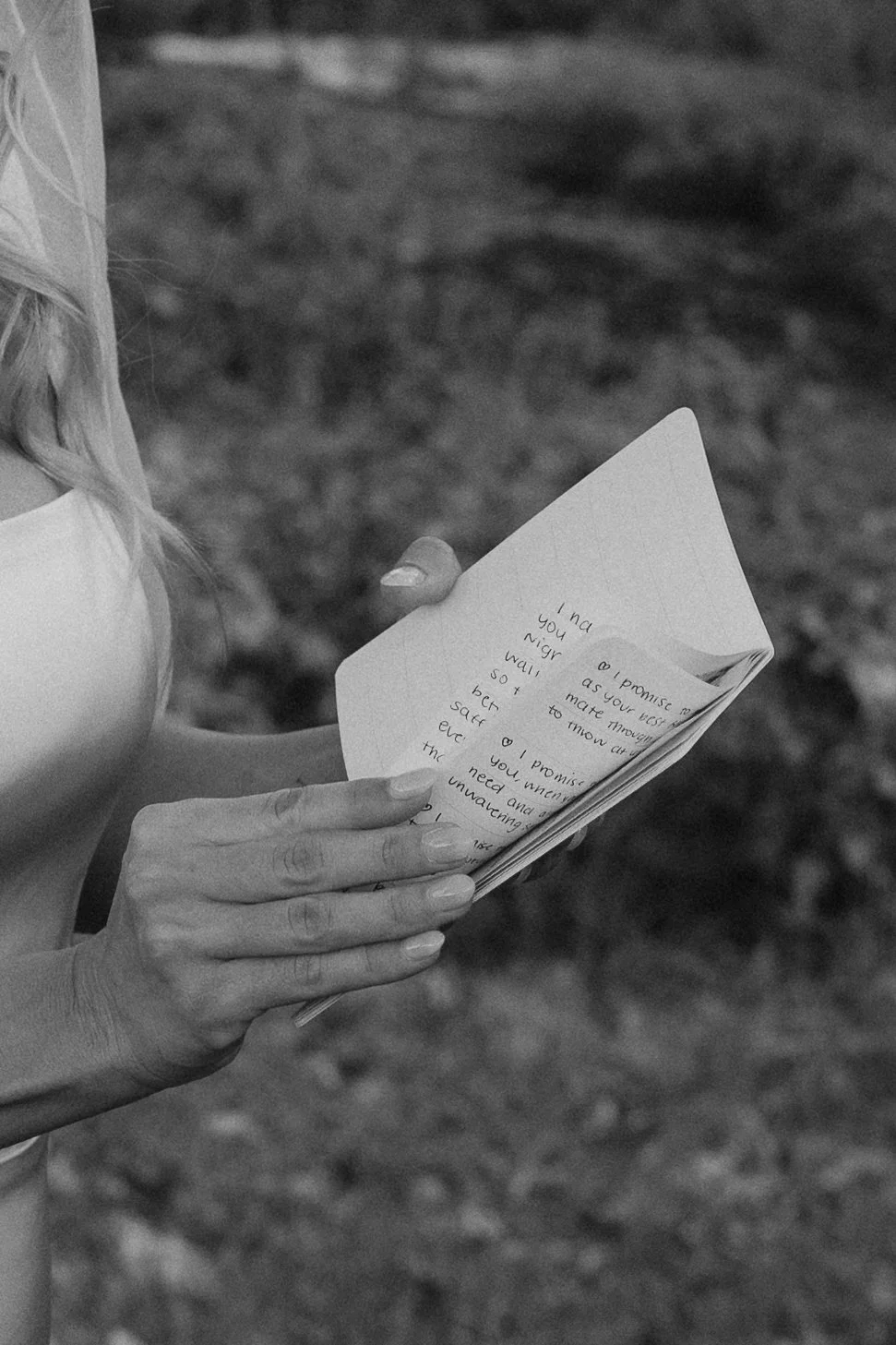 A woman with long hair reading a handwritten letter outdoors on a partly cloudy day.