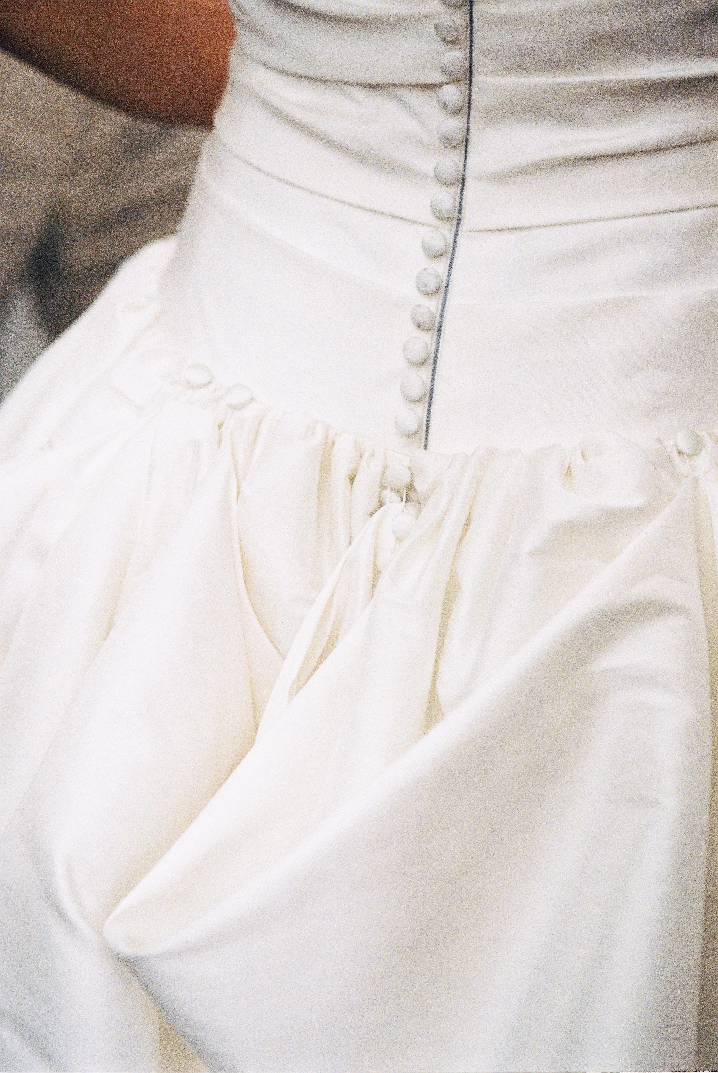 Close-up of a white wedding dress with buttons and a gathered skirt.