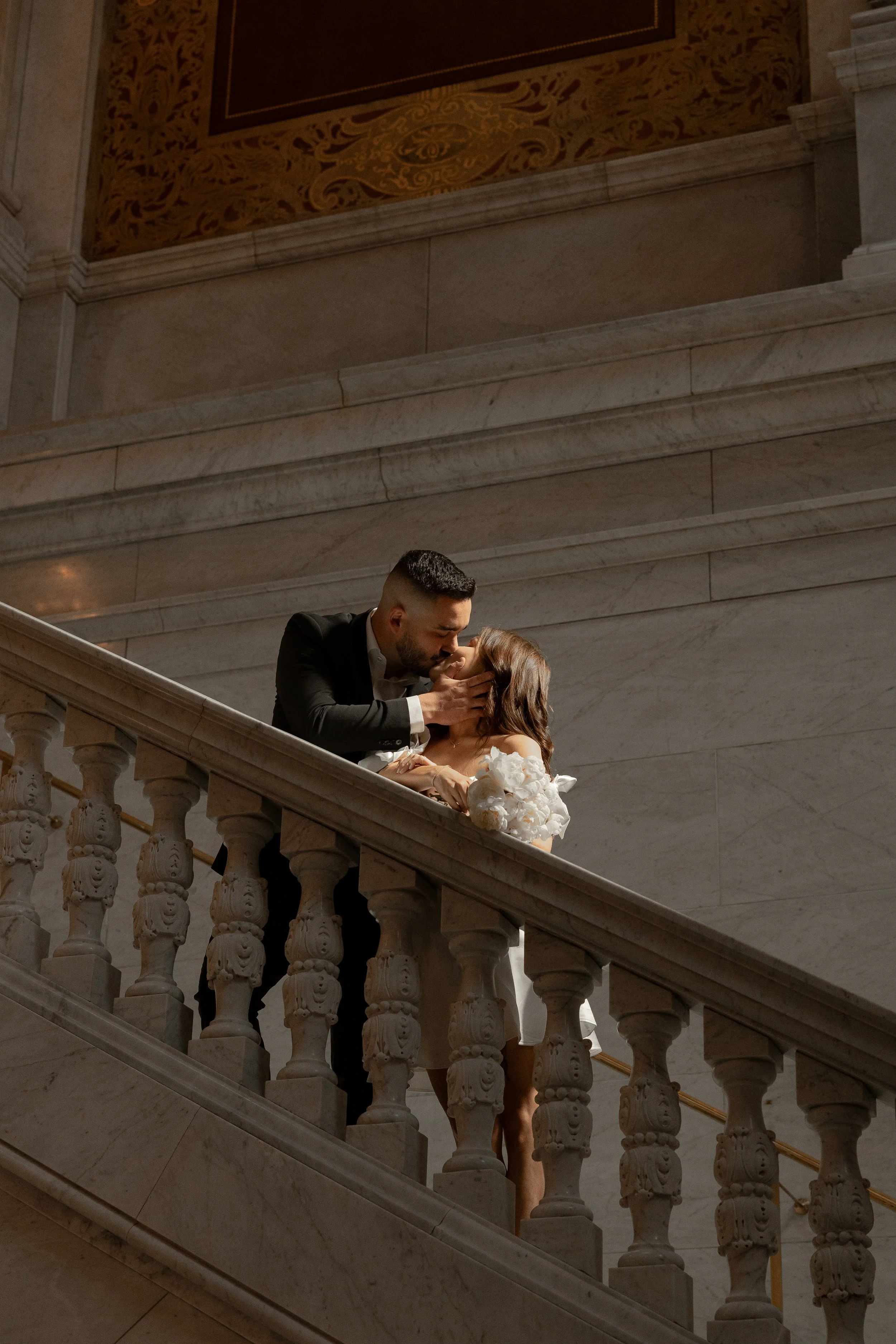 A man and woman sharing a kiss on a marble staircase inside a grand building.