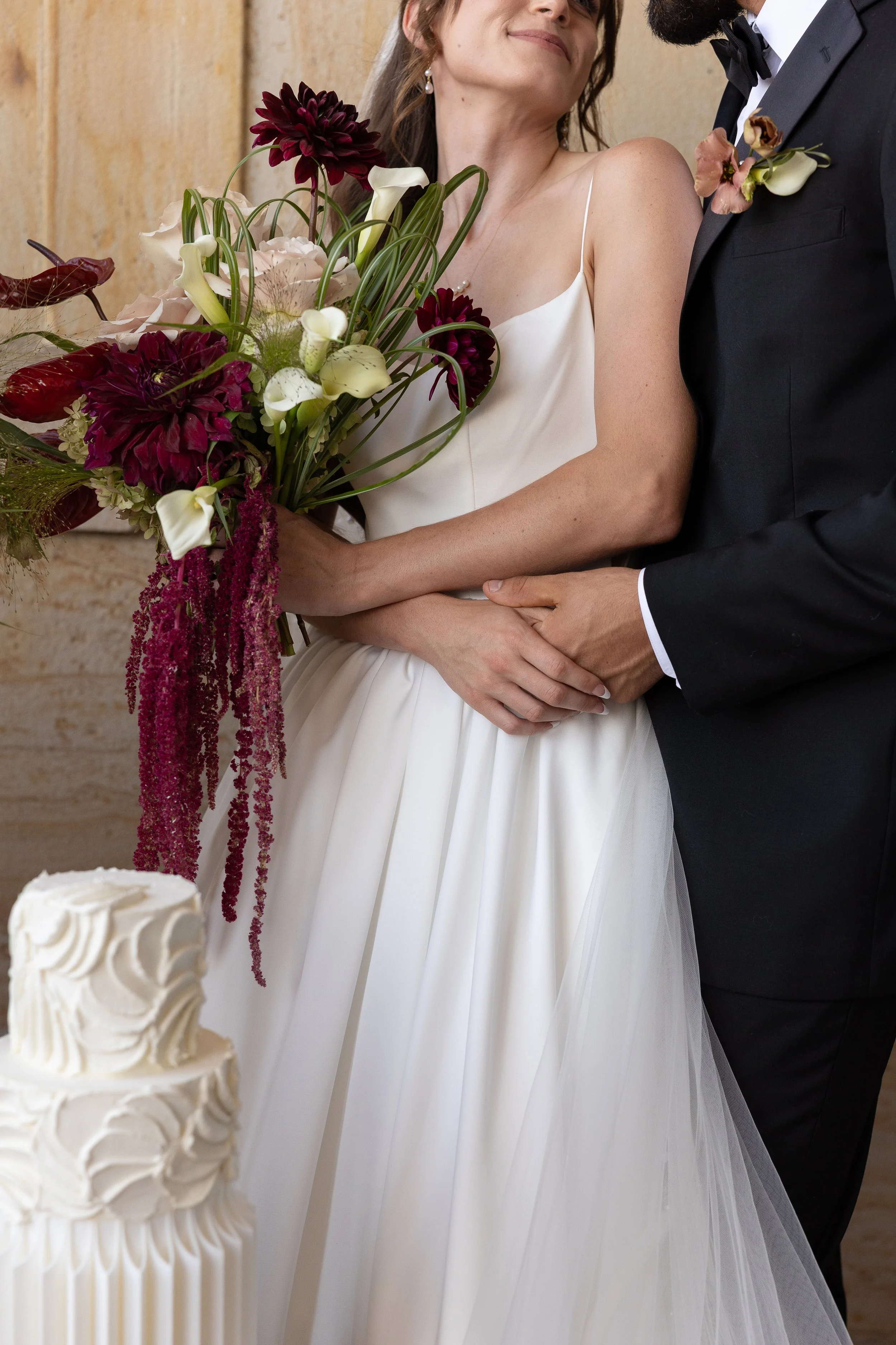 A bride and groom holding hands during their wedding, with the bride holding a large bouquet of flowers and a wedding cake in the foreground.