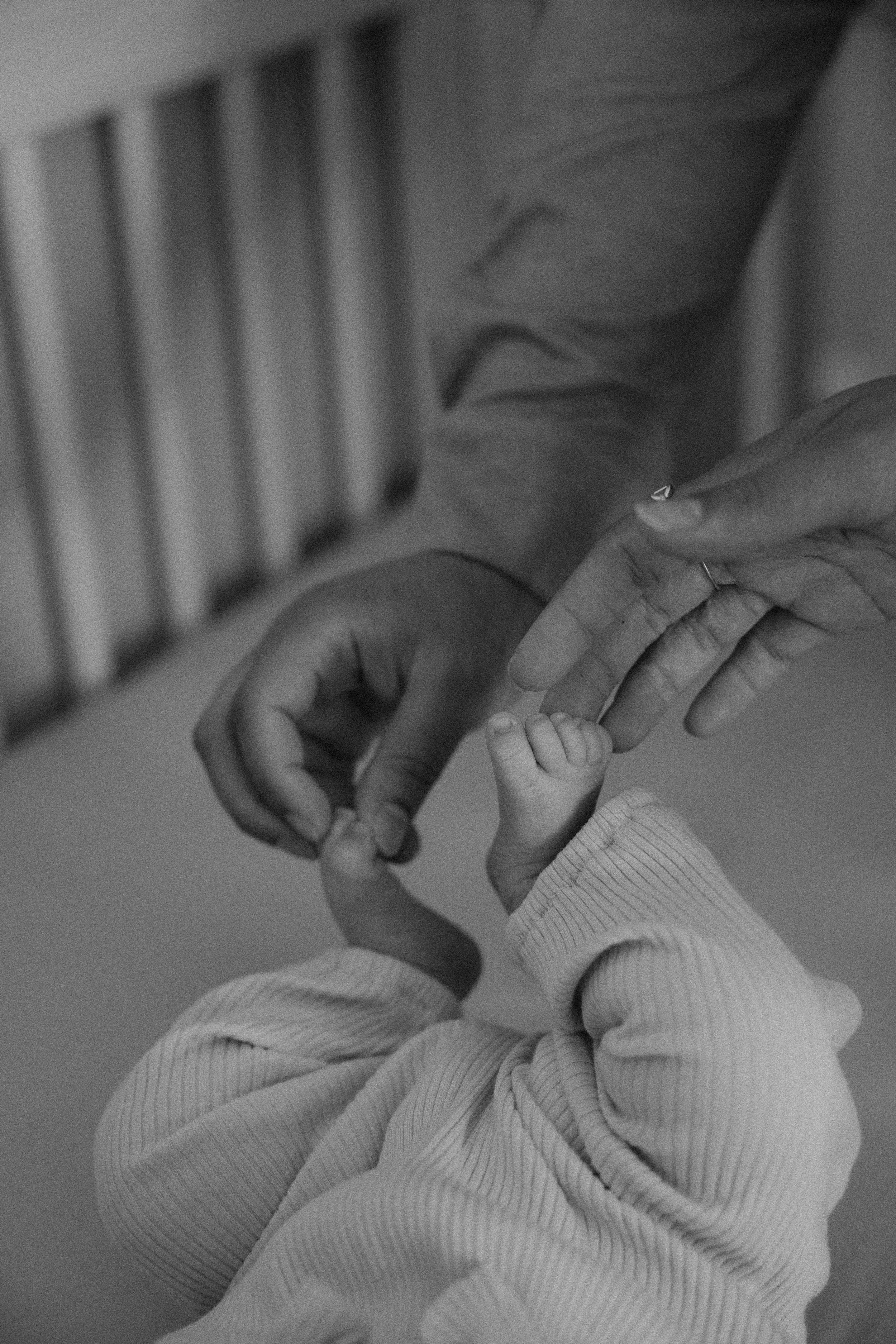 A close-up of a baby's hand holding an adult's finger, with the adult's other hand gently supporting the baby's hand.
