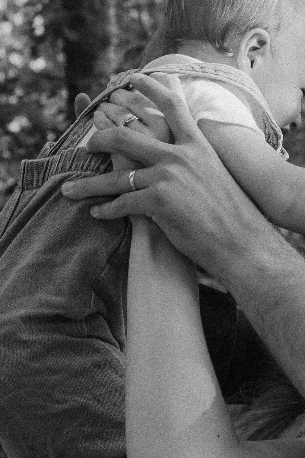 A person holding a small child close, with the child wrapping their arms around the person's neck, in a black-and-white photo.